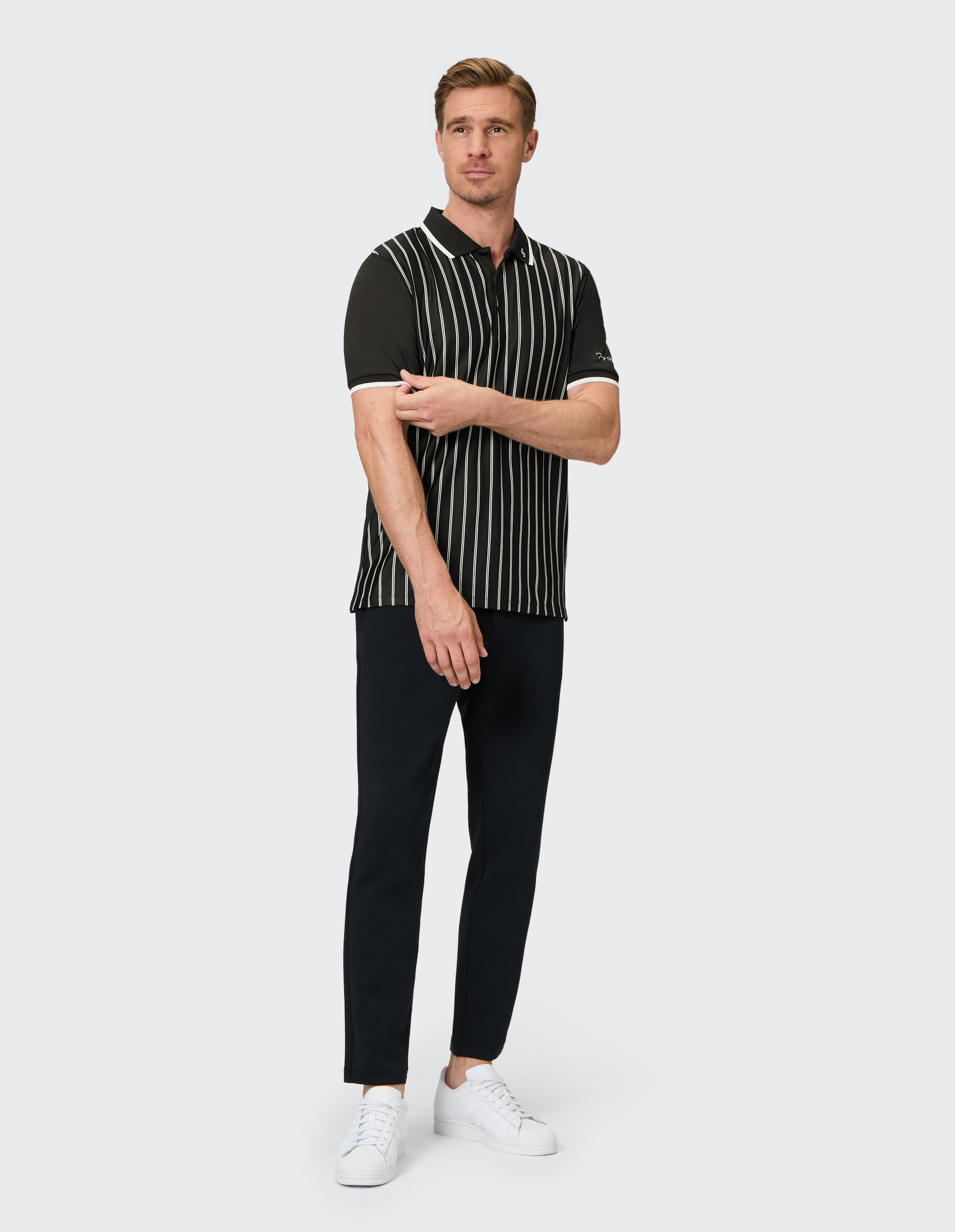 Mann trägt ein schwarz gestreiftes Poloshirt und eine dunkle Hose für einen klassischen Freizeitlook.