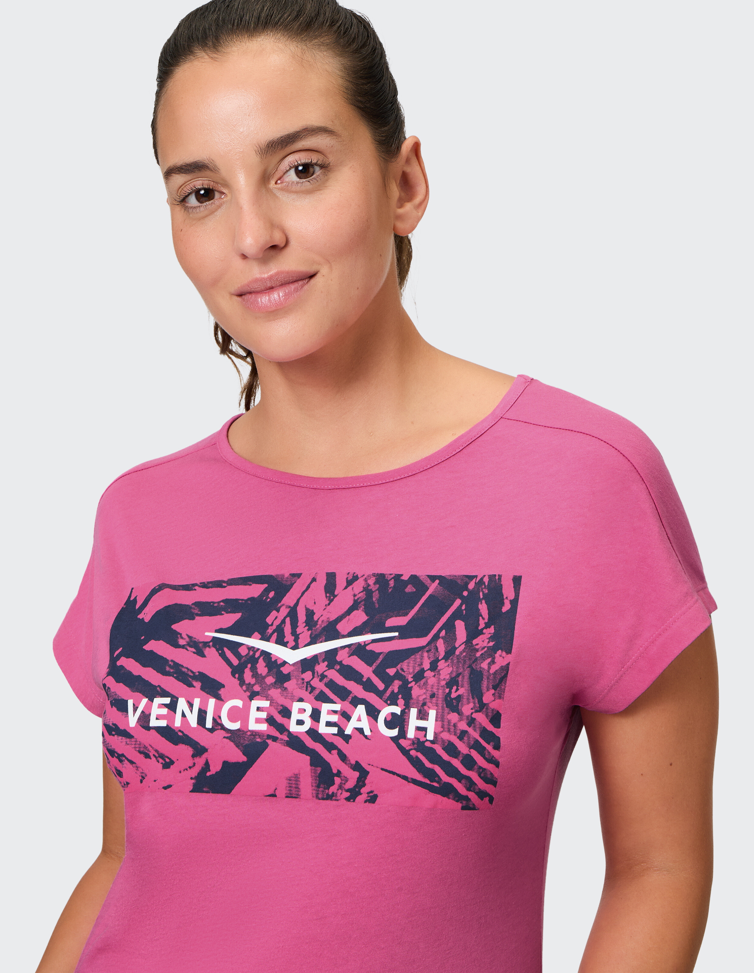 Frau trägt ein rosa T-Shirt mit Venice Beach-Grafik für lässigen, bequemen Stil.