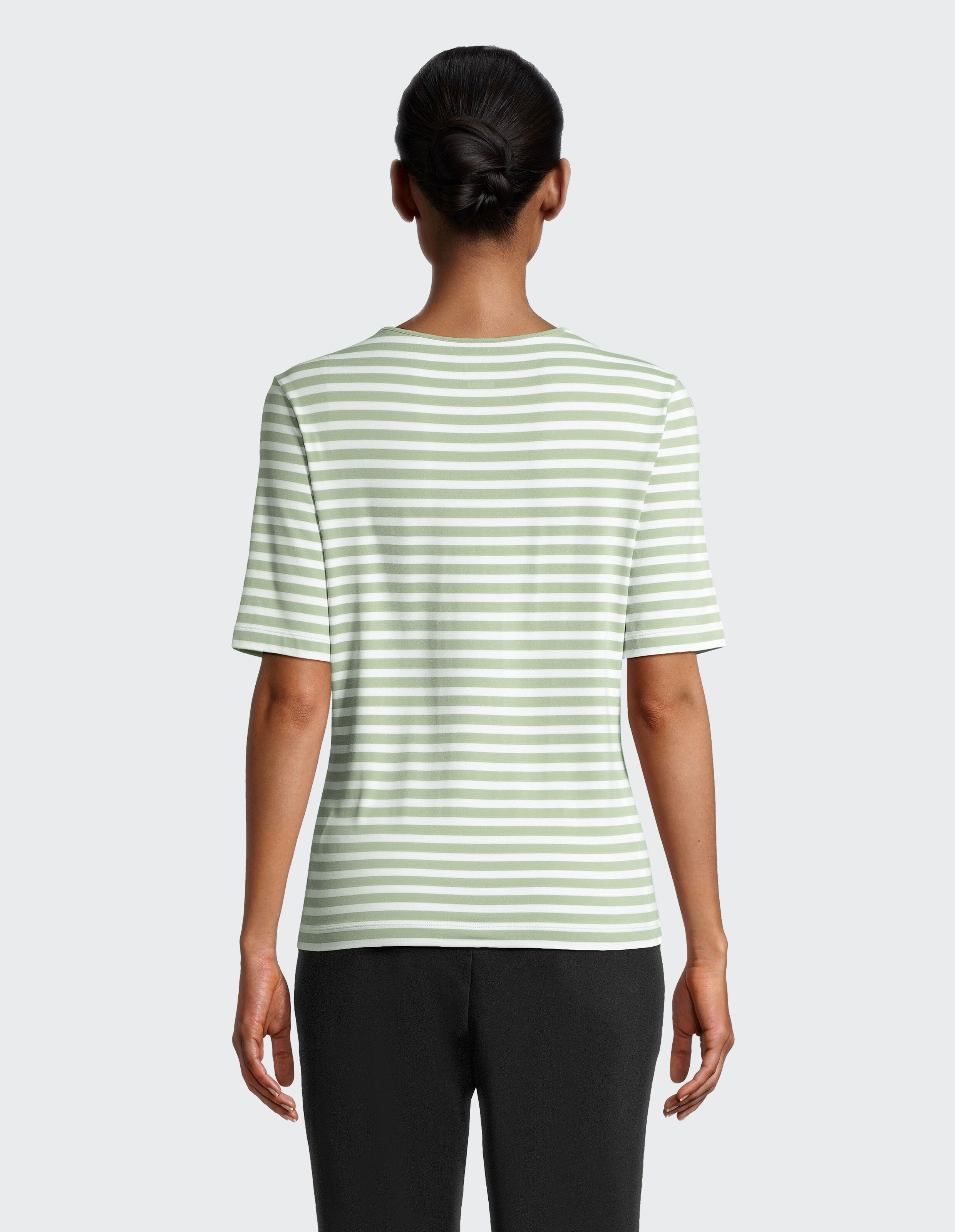 Person von hinten in grün-weiß gestreiftem Shirt und schwarzer Hose, das Haar ist ordentlich zum Knoten gebunden.
