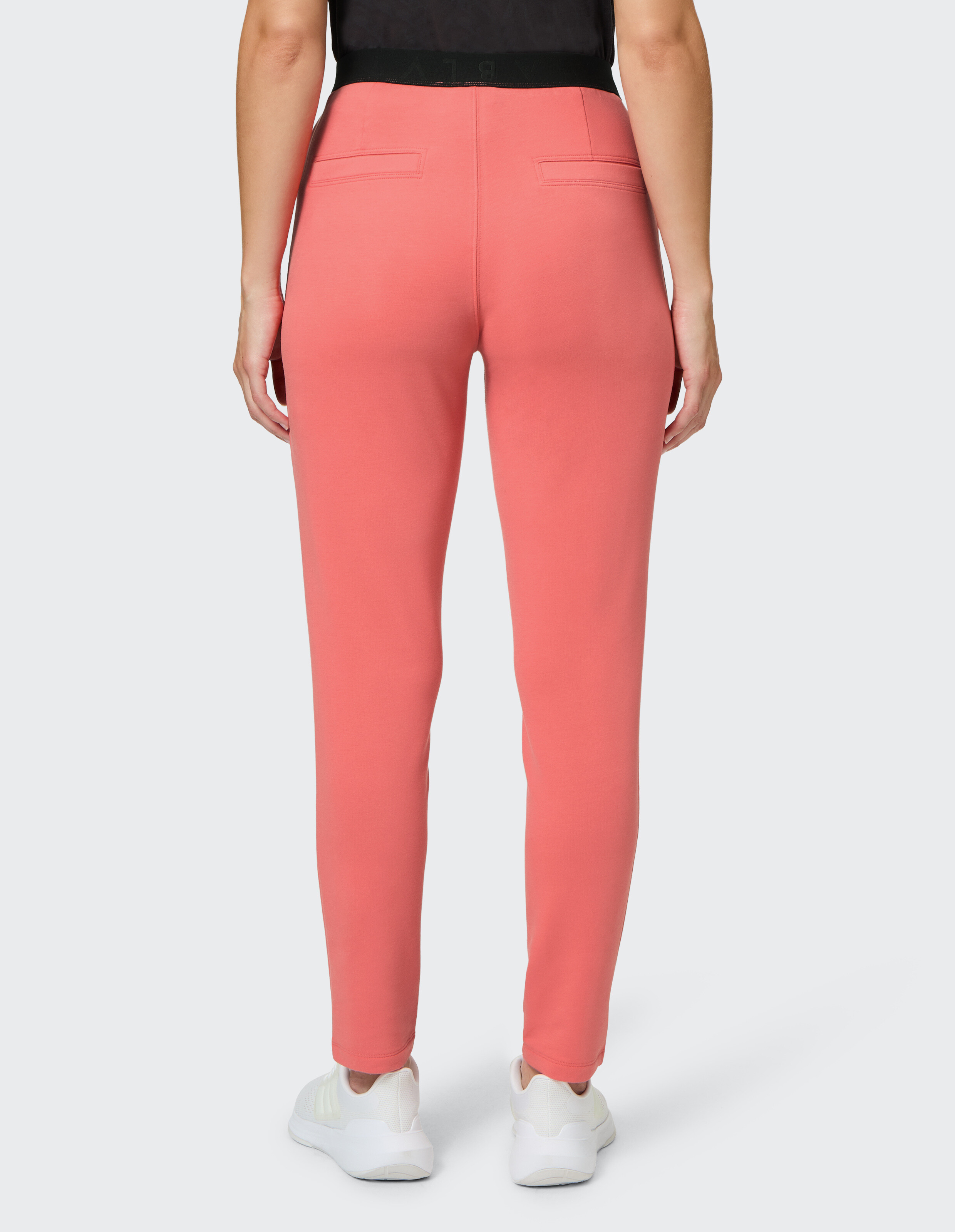 Rückansicht einer korallenroten Freizeithose mit schwarzem elastischem Bund und weißen Turnschuhen.