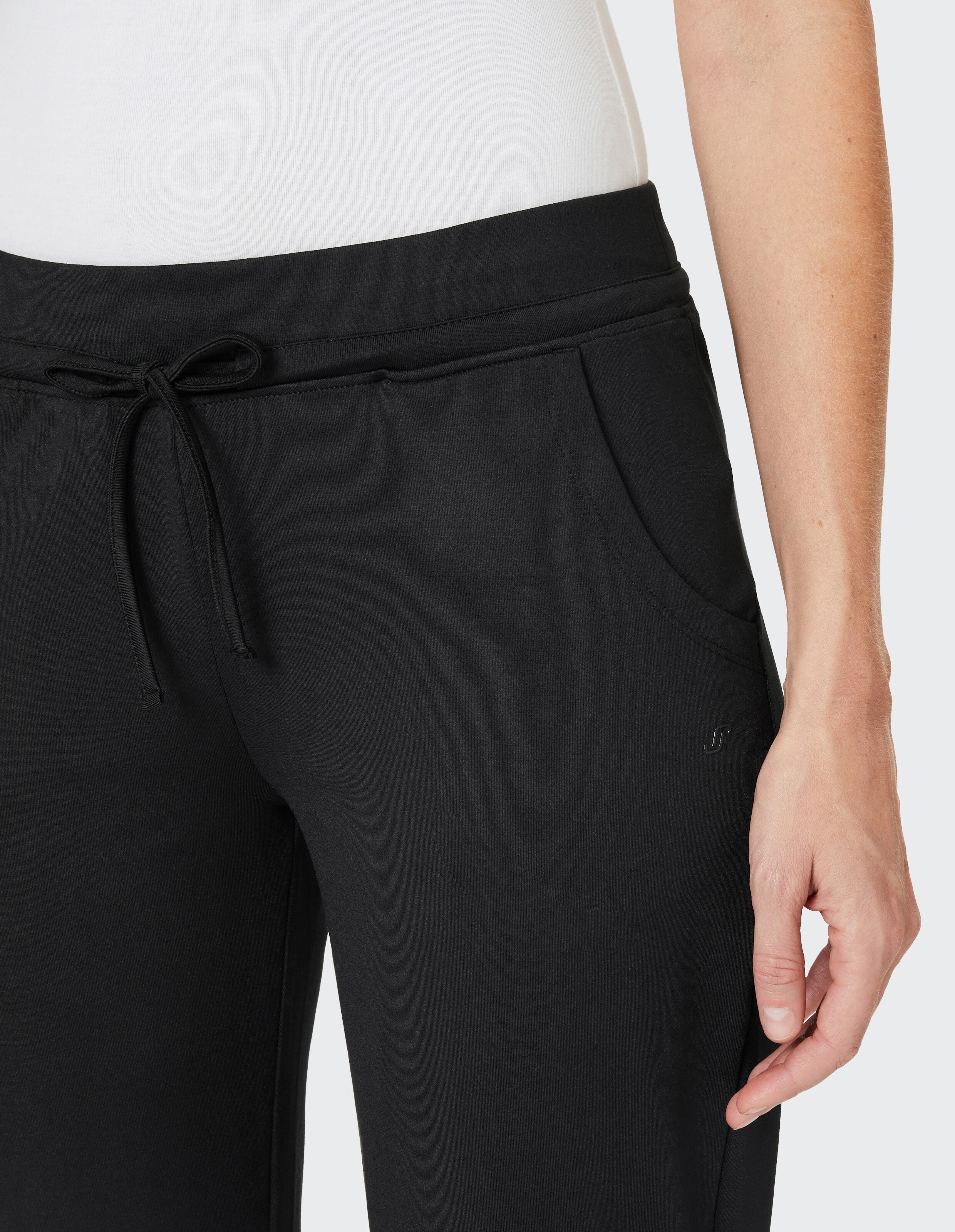 Eine Person trägt eine schwarze Jogginghose mit Kordelzug und Seitentaschen, kombiniert mit einem weißen Oberteil.