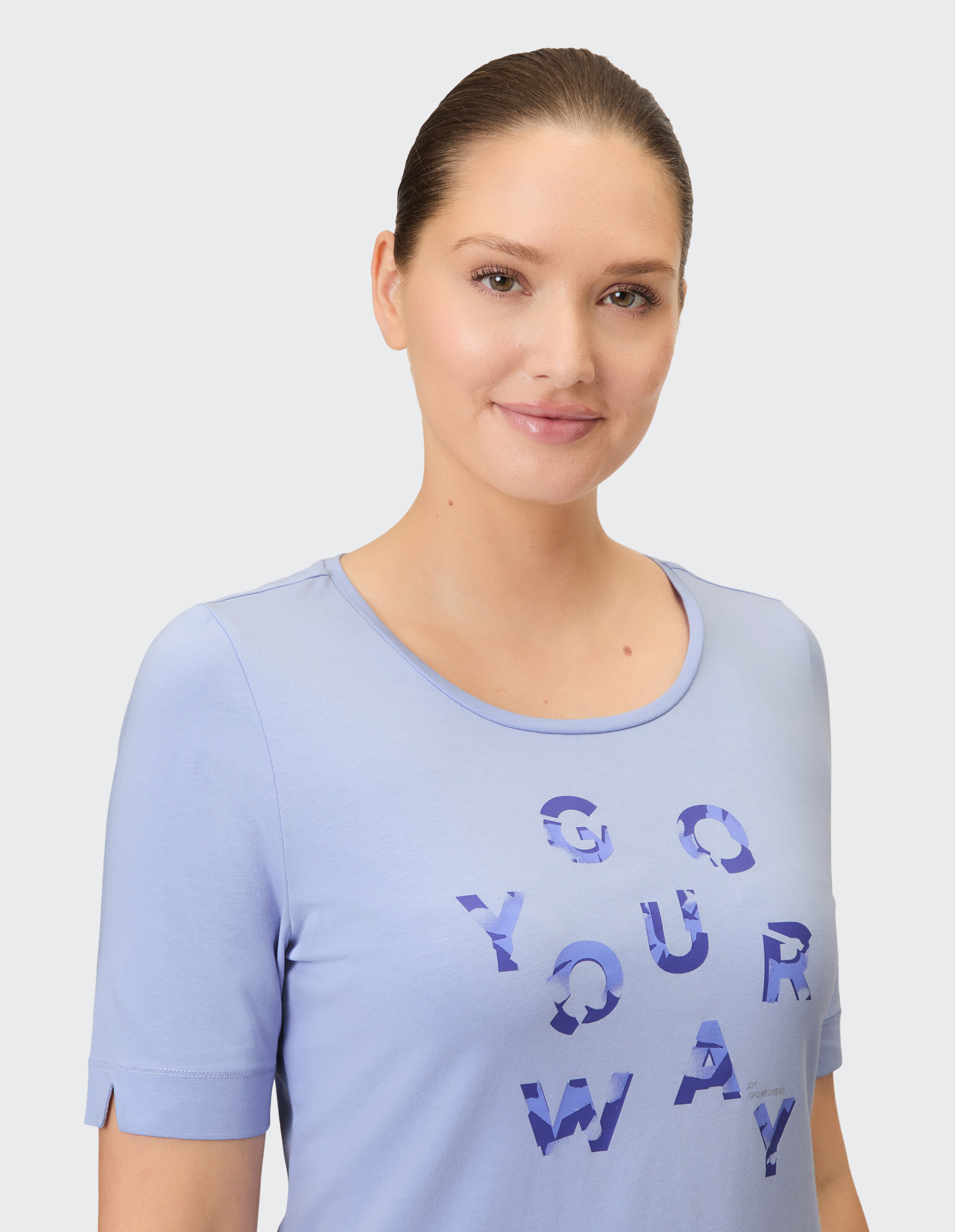 Eine Frau trägt ein hellblaues Kurzarmshirt mit dem Schriftzug "GO YOUR WAY" in dunkleren Blau-Tönen.