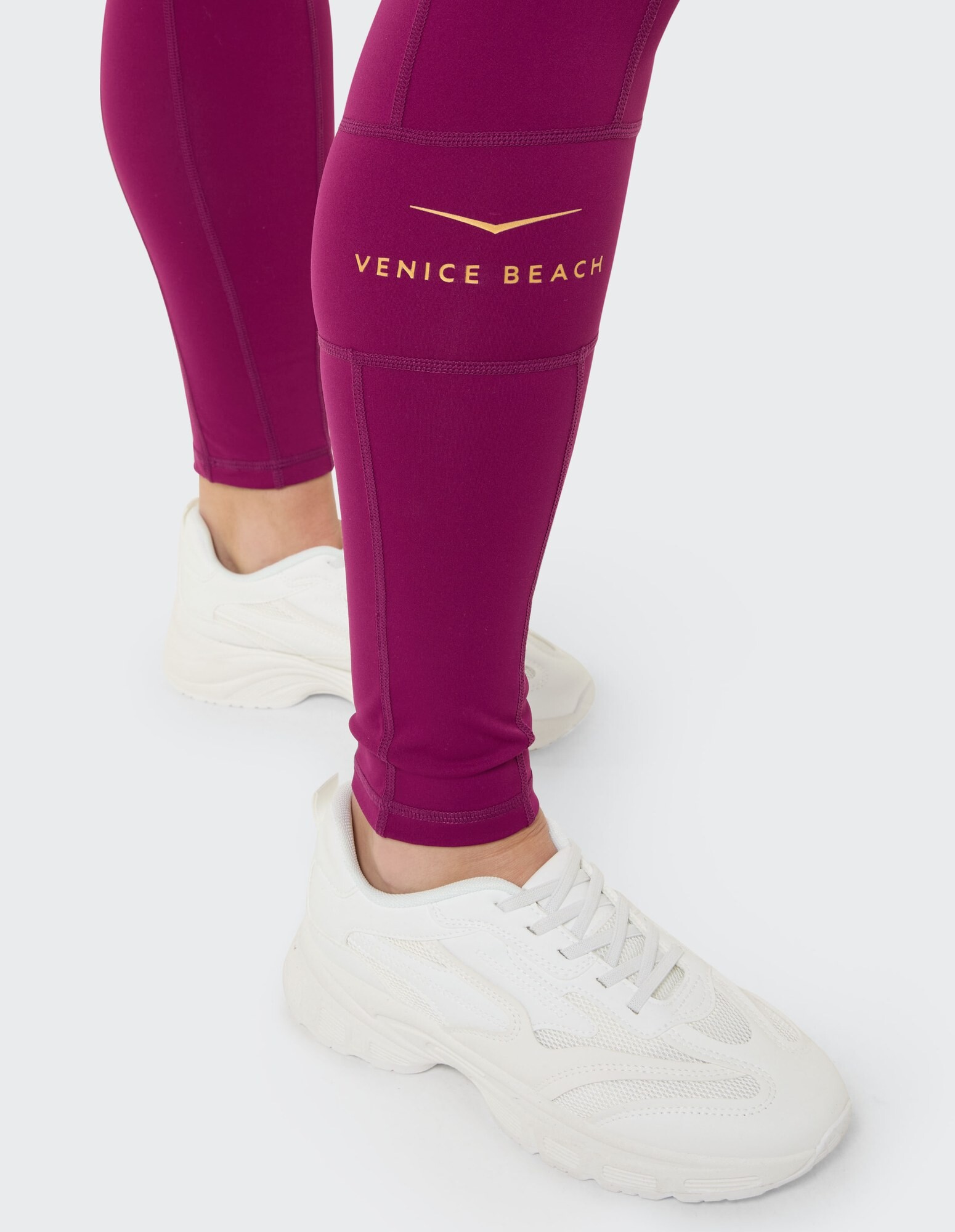 Nahaufnahme einer burgunderfarbenen Leggings mit „Venice Beach“-Logo und weißen Turnschuhen.