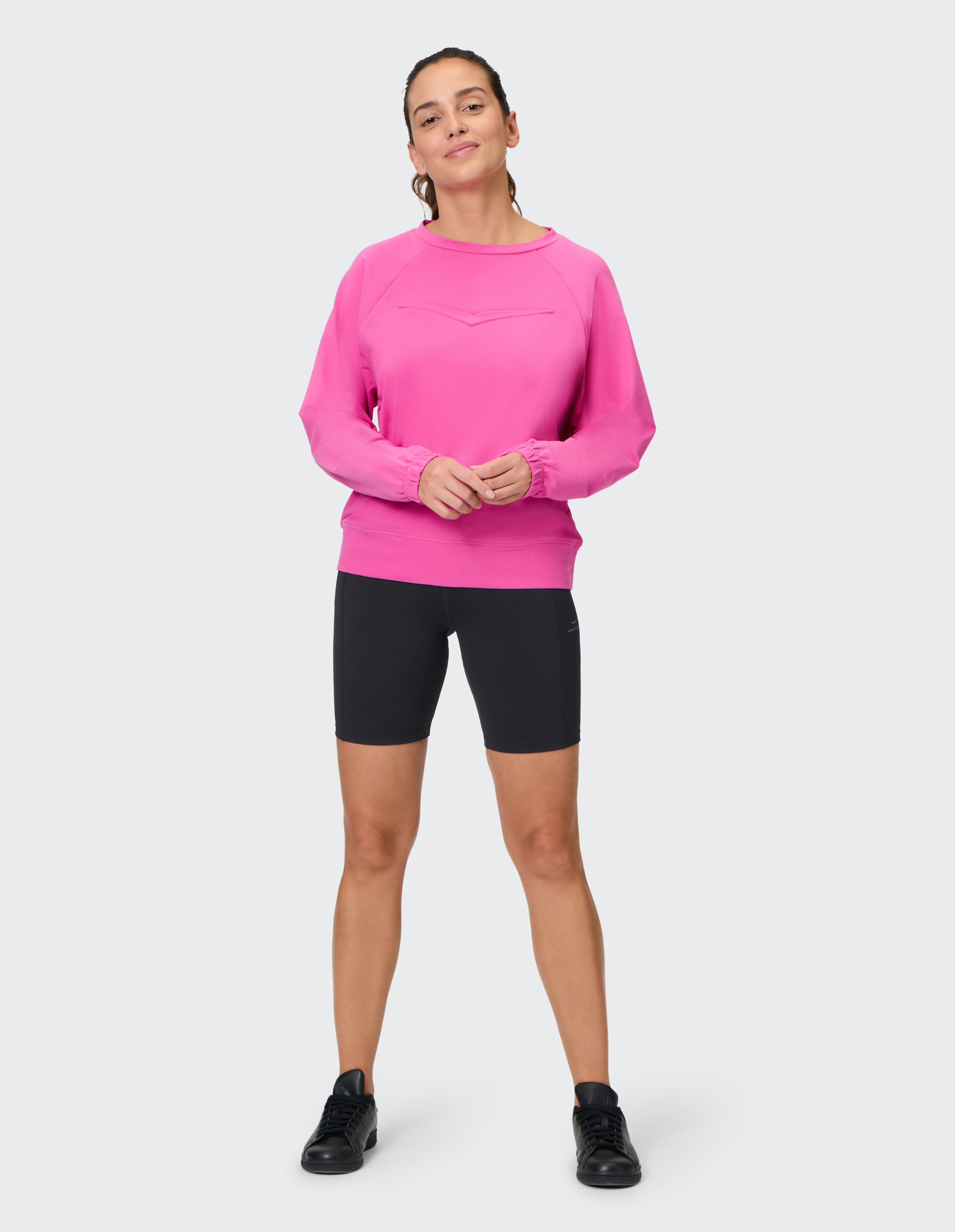 Frau in einem rosa Sweatshirt und schwarzen Fahrradshorts, die lässigen Komfort zur Schau stellt.