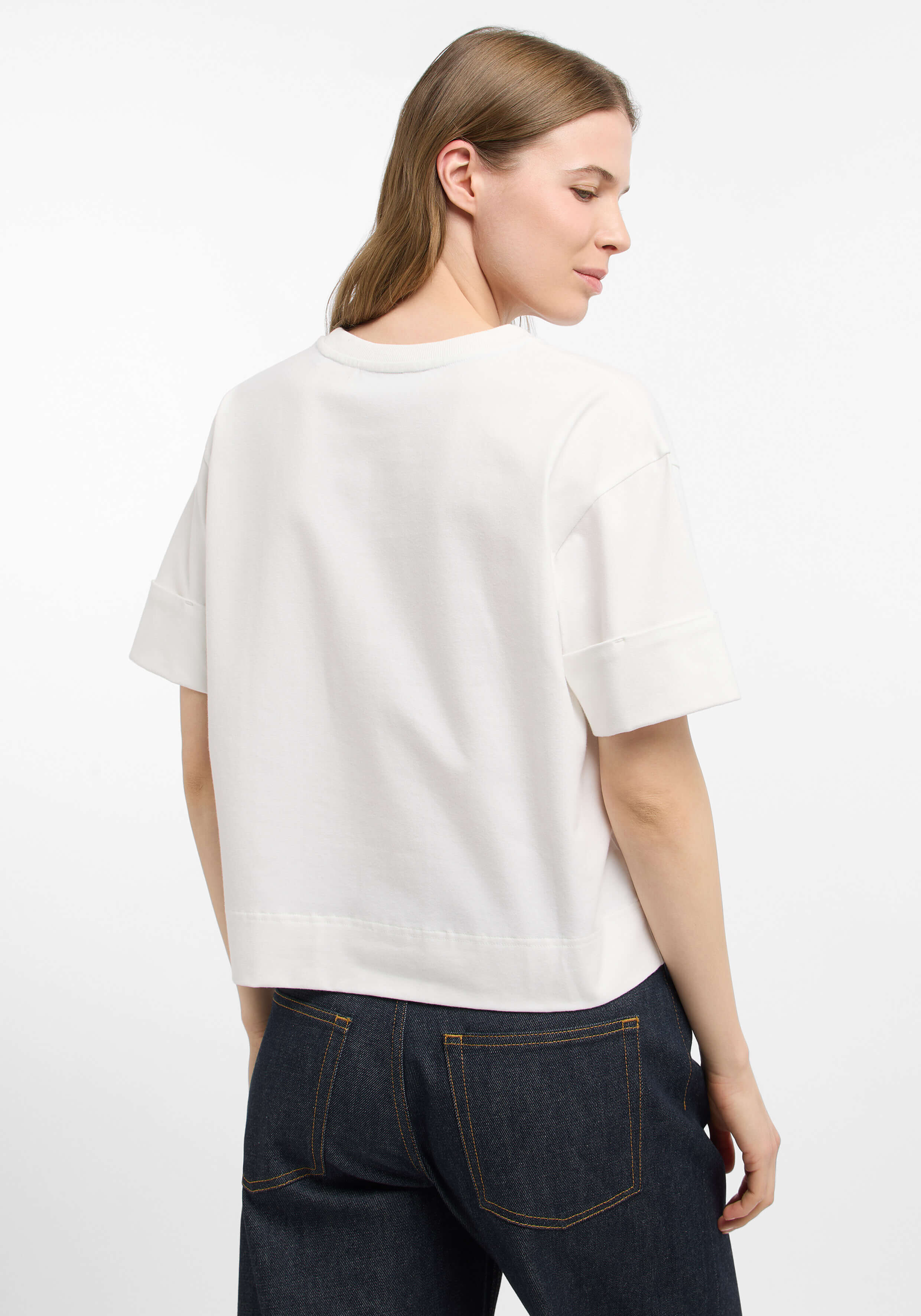 Frau trägt ein weißes, lässiges Kurzarm-T-Shirt mit Bündchen an den Ärmeln und dunkle Jeans.