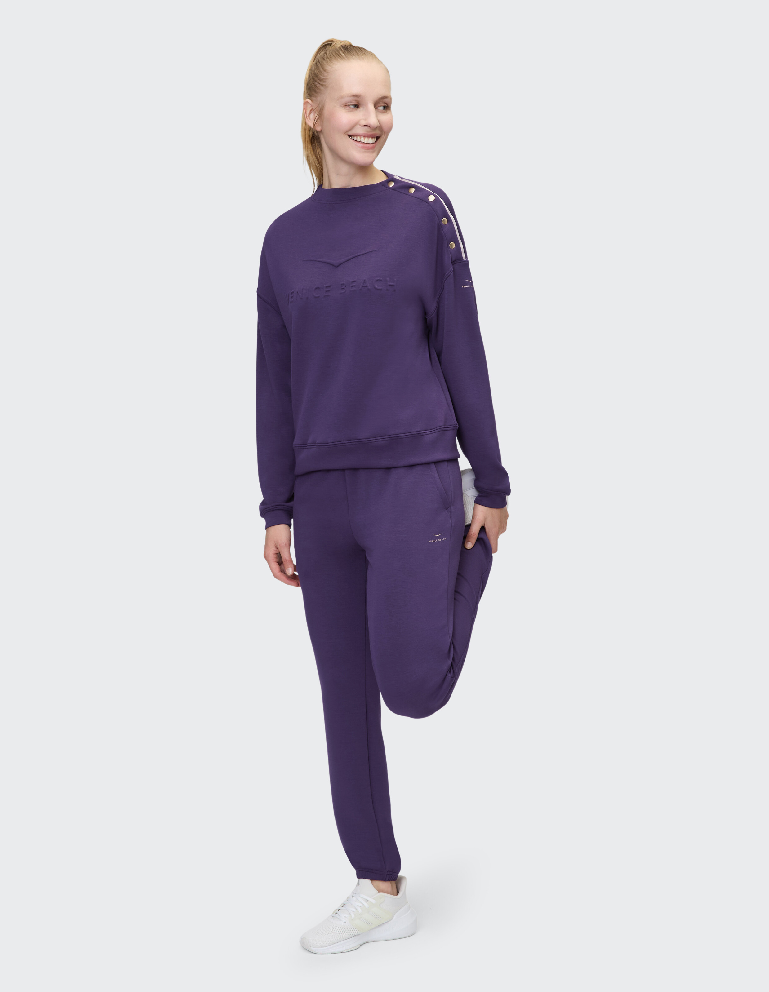 Frau in lila lässigem Sweatshirt und Hose, die einen bequemen, stilvollen Look präsentiert.