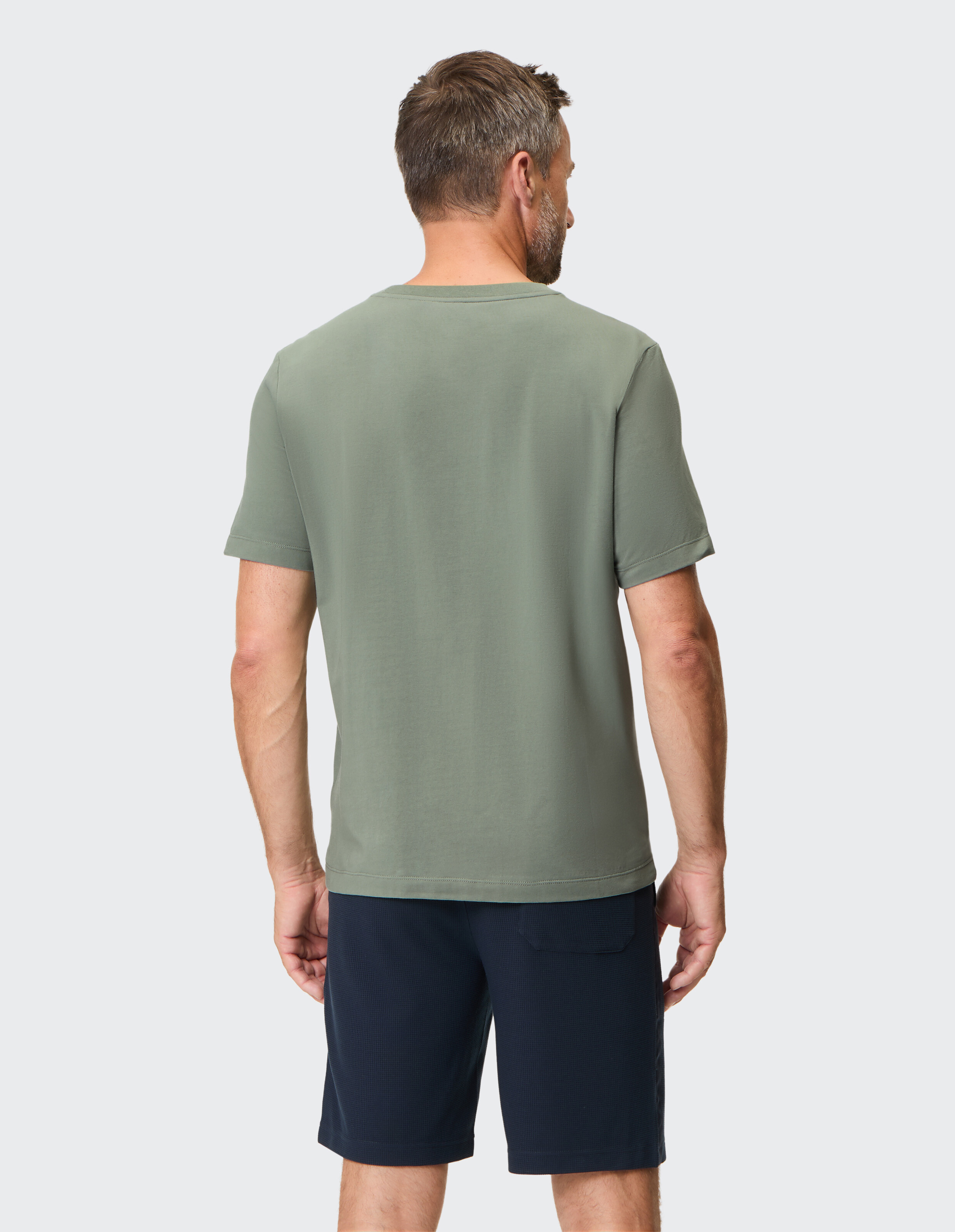 Mann trägt ein salbeigrünes T-Shirt mit Rundhalsausschnitt und dunkelblaue Shorts für einen lässigen Sommerstil.