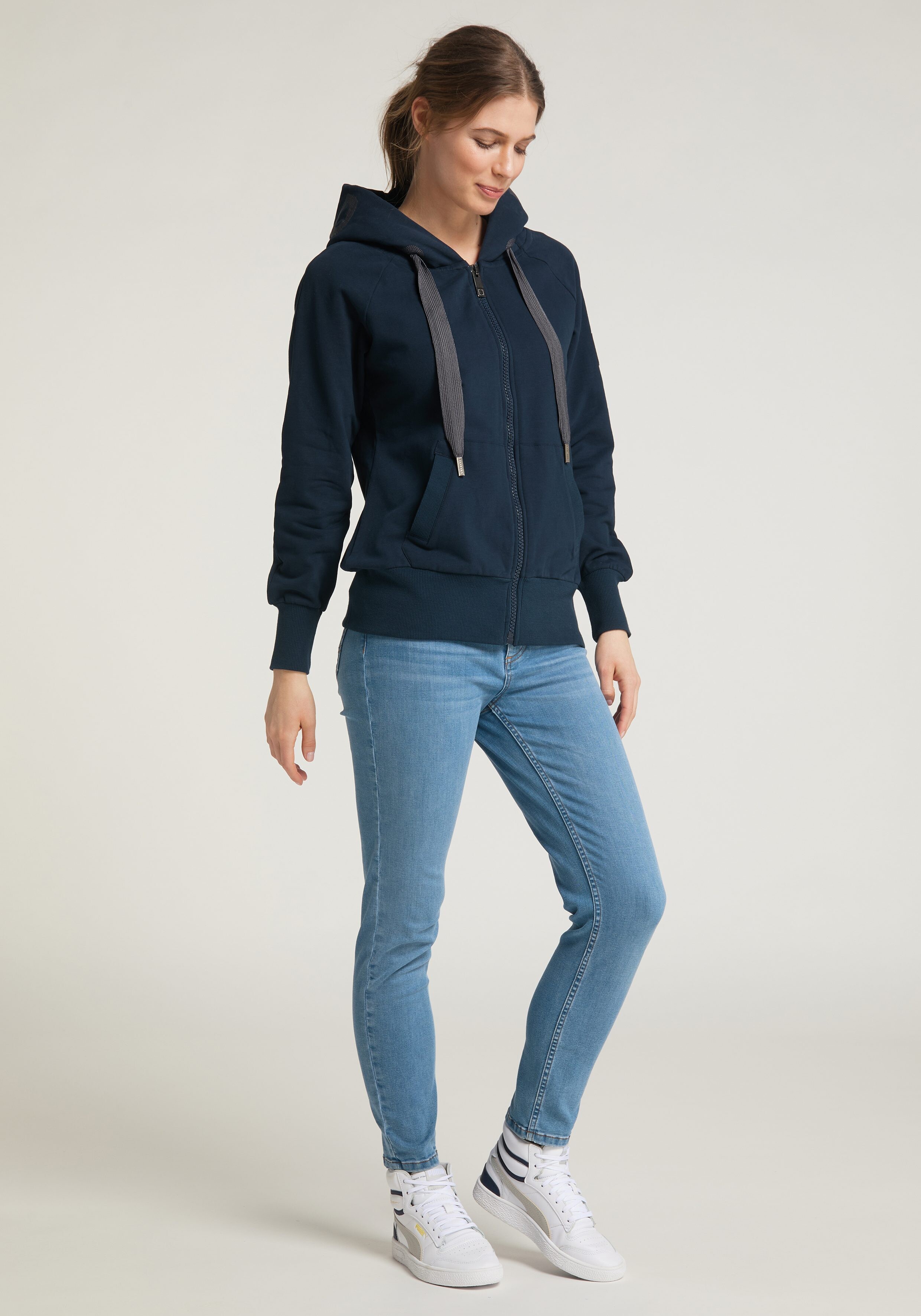 Frau trägt einen gemütlichen marineblauen Kapuzenpullover mit Reißverschluss und hellblaue Jeans für einen lässigen Alltagsstil.