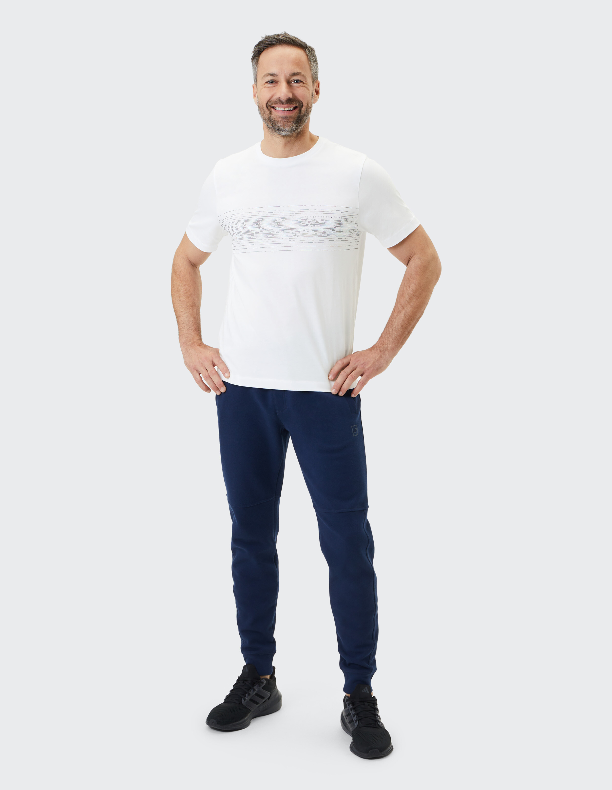 Mann trägt ein weißes Grafik-T-Shirt und eine dunkelblaue Jogginghose für einen lässigen Look.