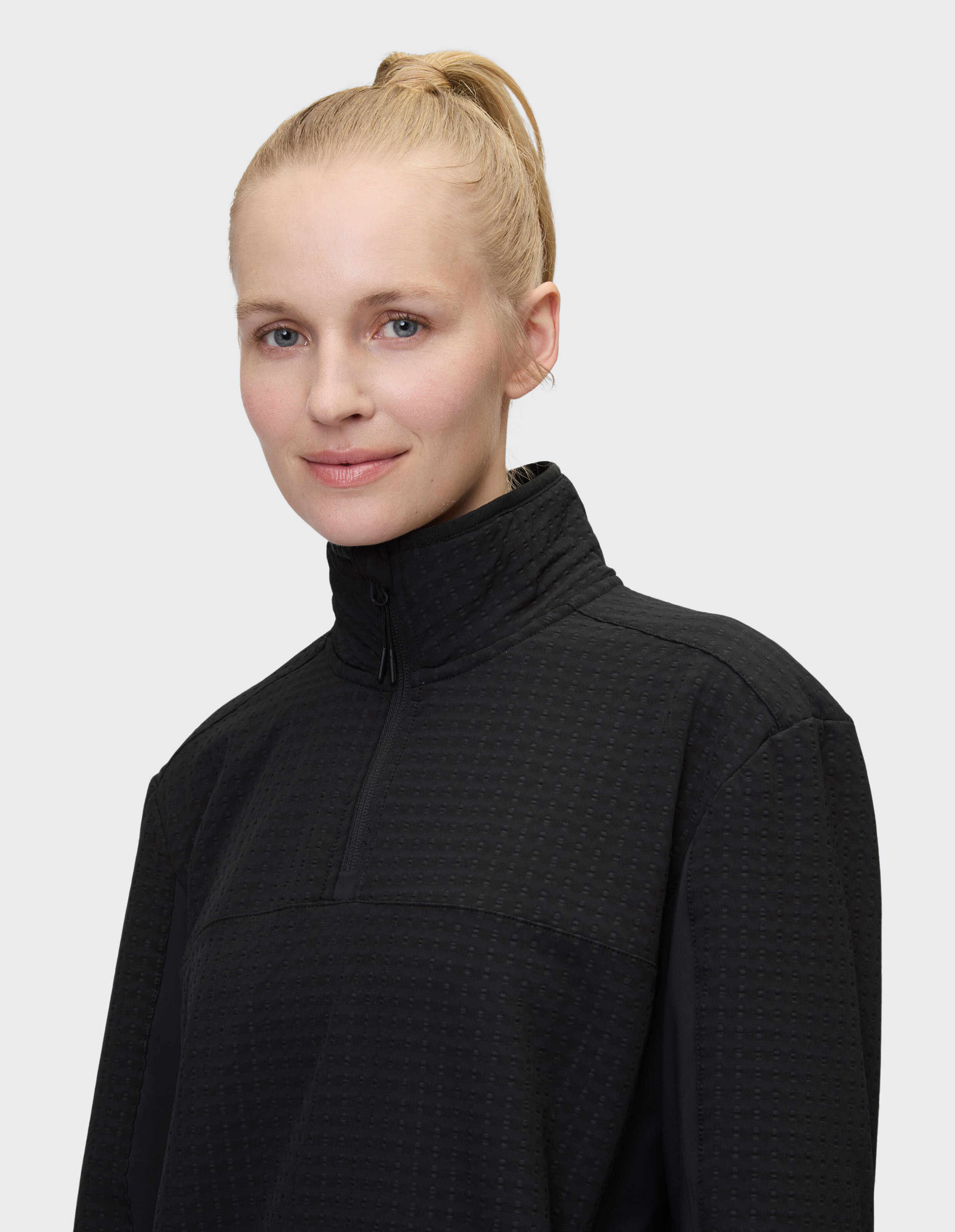 Frau trägt einen schwarzen, strukturierten Pullover mit Viertelreißverschluss für einen gemütlichen, lässigen Stil.