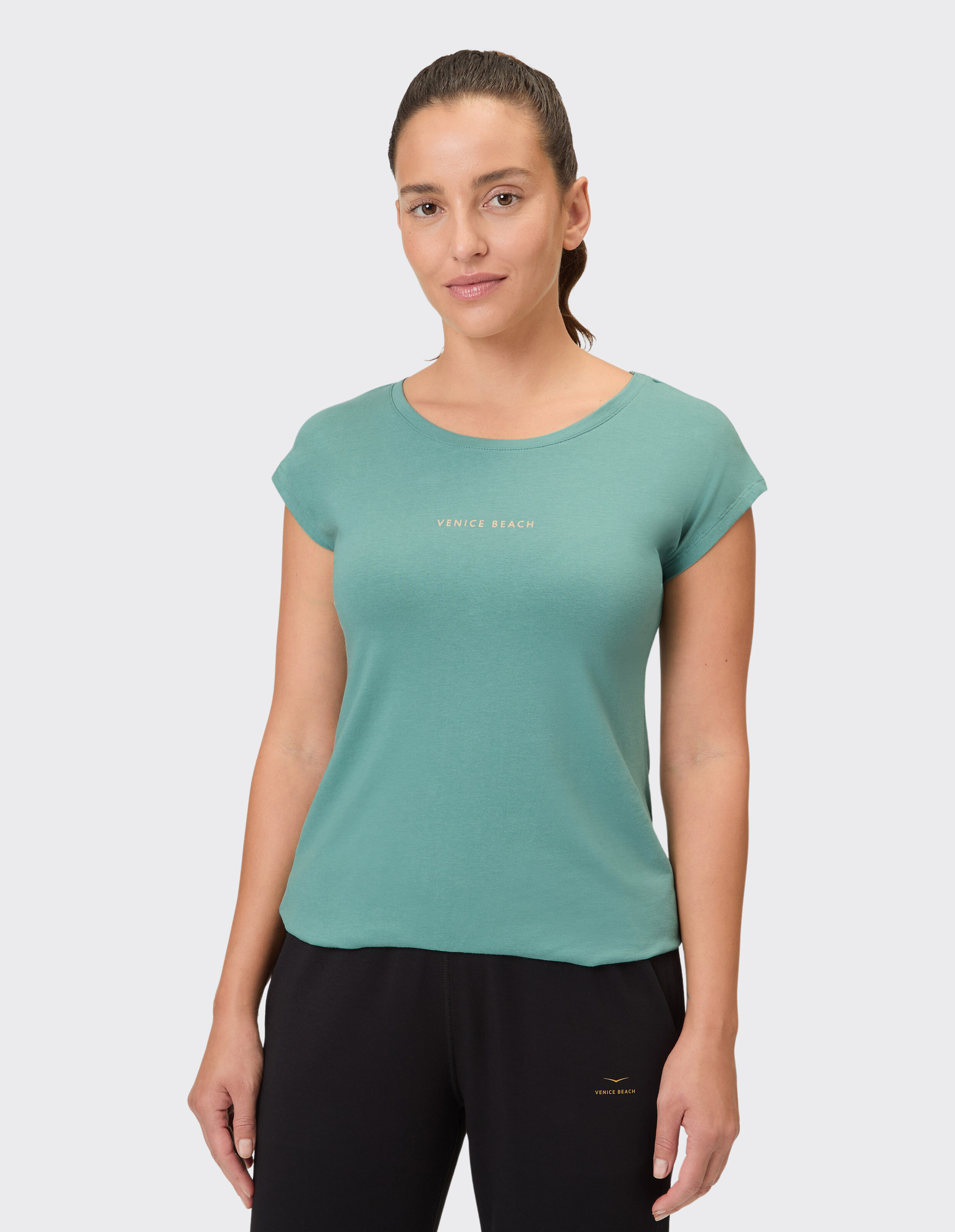 Frau trägt ein grünes lässiges T-Shirt von Venice Beach und eine schwarze Loungehose.