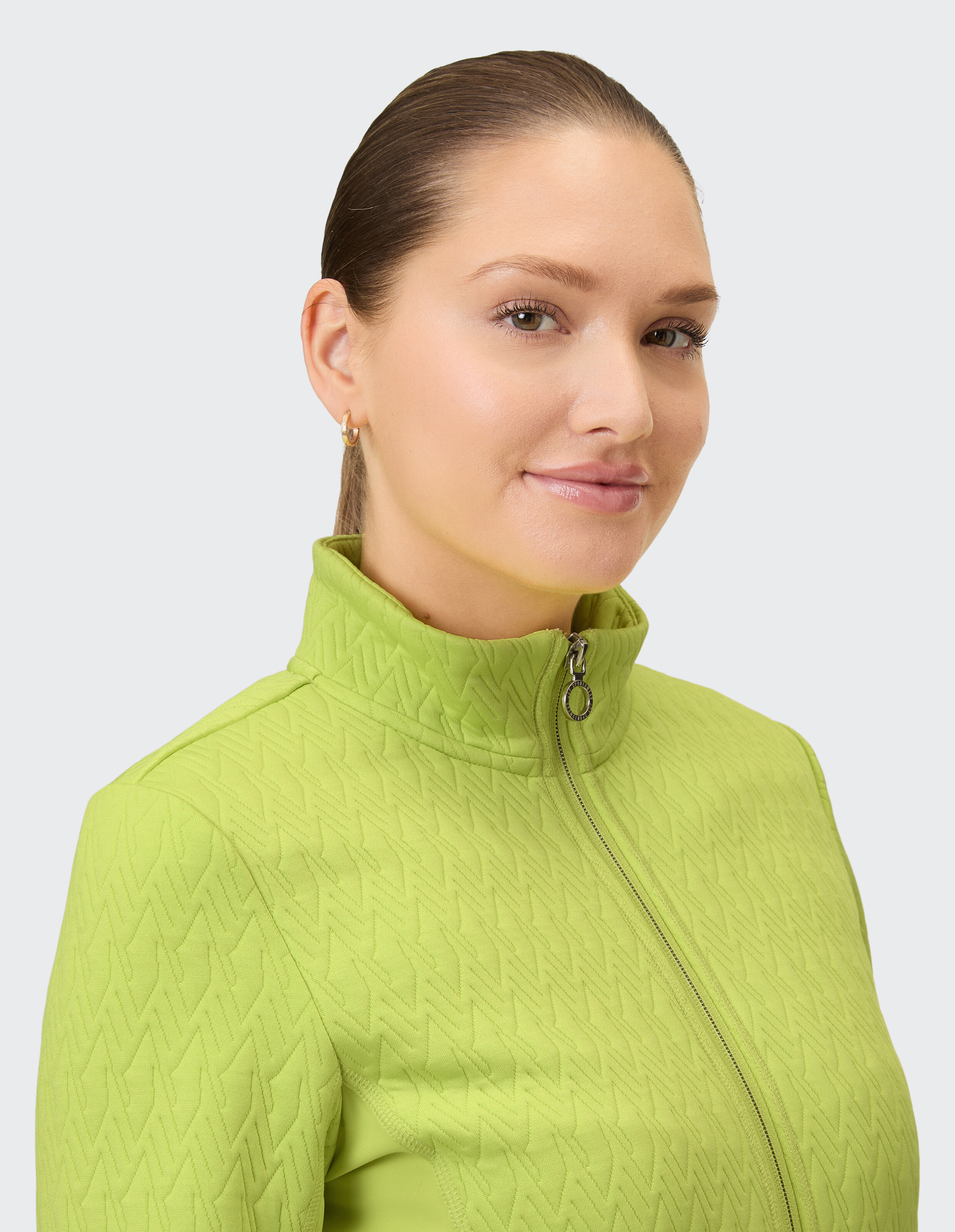 Eine Frau trägt eine leuchtend grüne Jacke mit einem gesteppten Zickzackmuster und einem Reißverschluss.