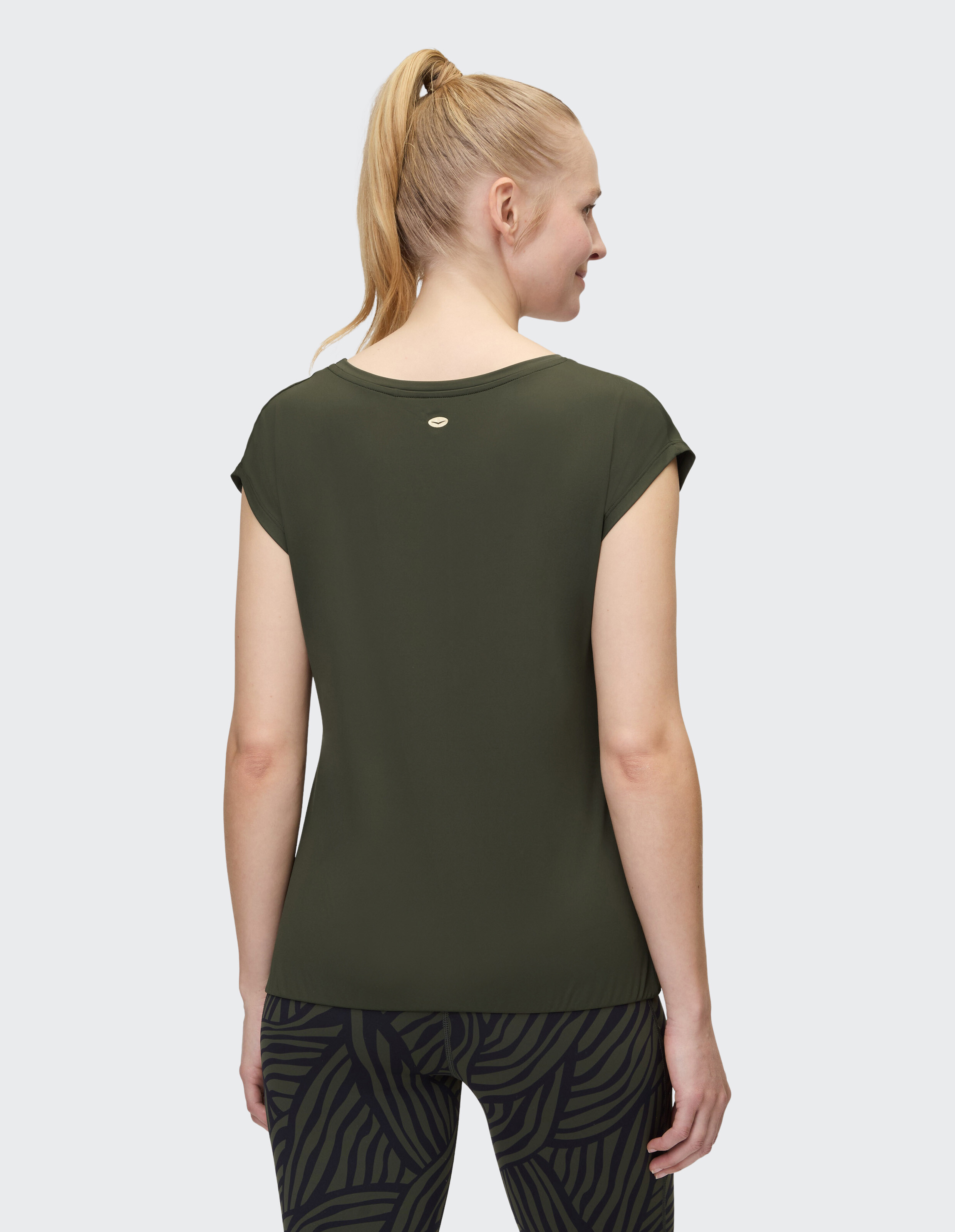 Rückansicht einer Frau in einem dunkelgrünen Freizeitoberteil und gemusterten Leggings.
