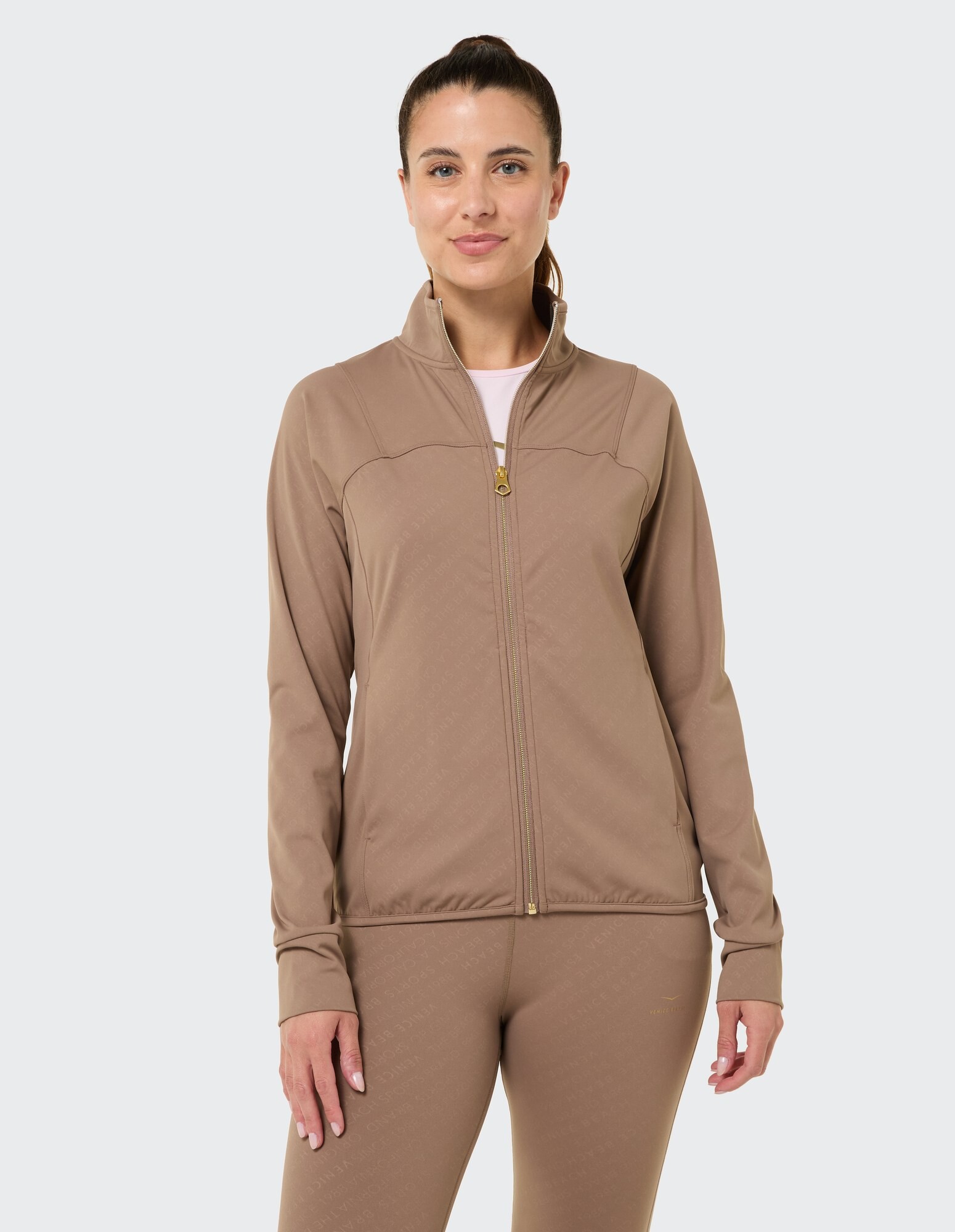Frau in einer braunen Jacke mit Reißverschluss und passenden Leggings, die lässigen Komfort ausstrahlt.
