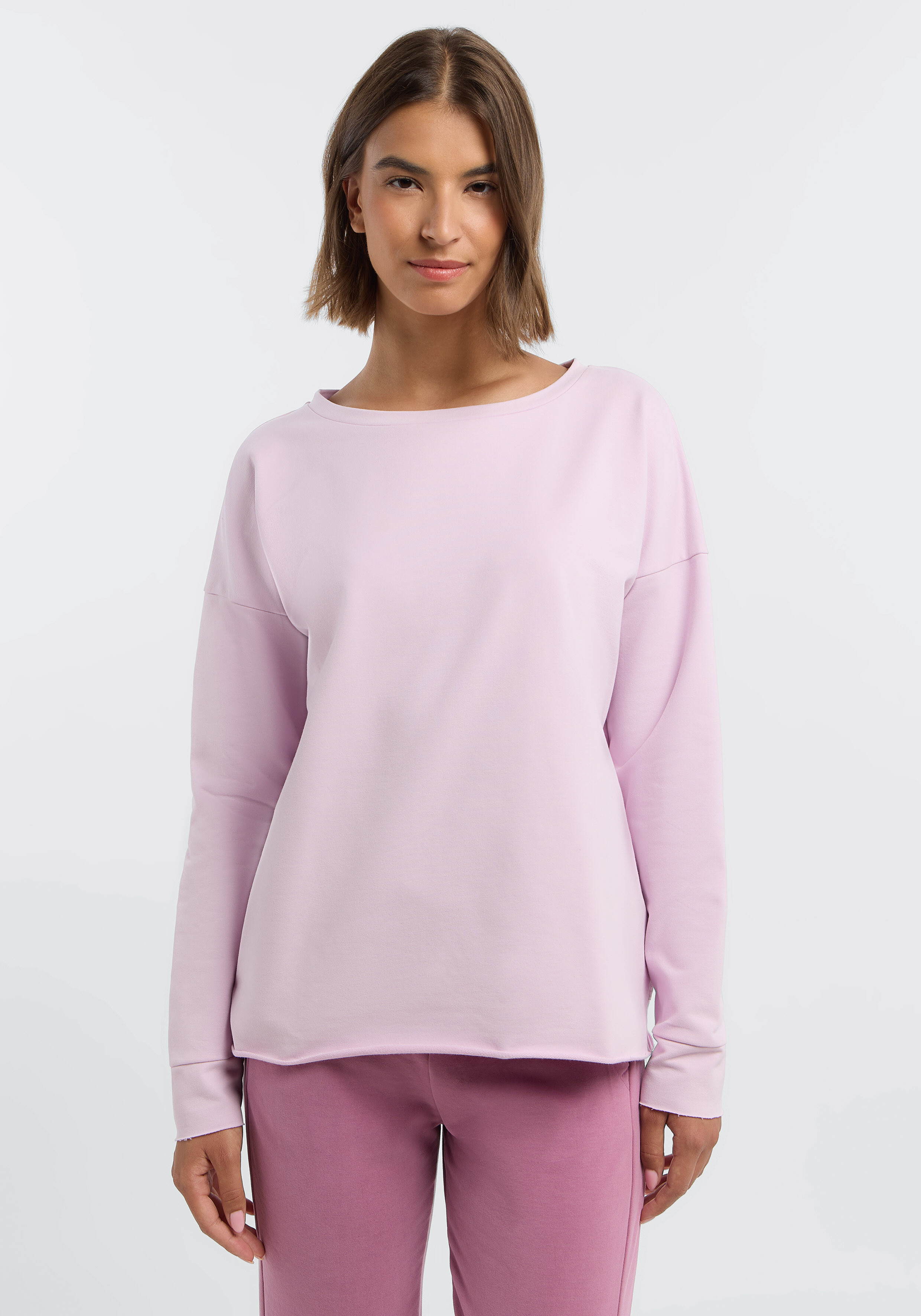 Frau trägt ein kuscheliges, hellrosa, langärmliges Freizeit-Sweatshirt zum Entspannen.