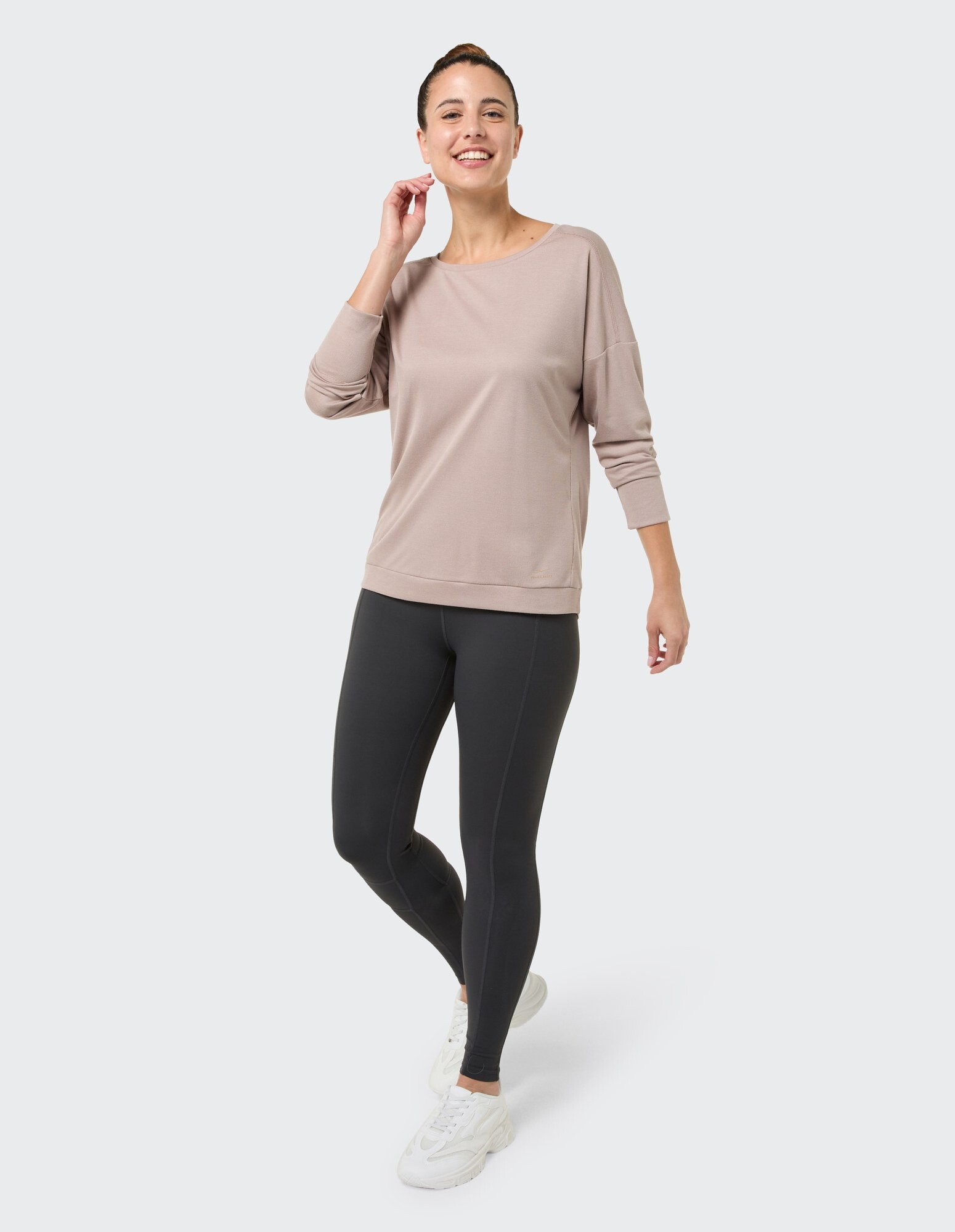 Frau in einem hellrosa Langarmshirt und schwarzen Leggings, lächelnd.
