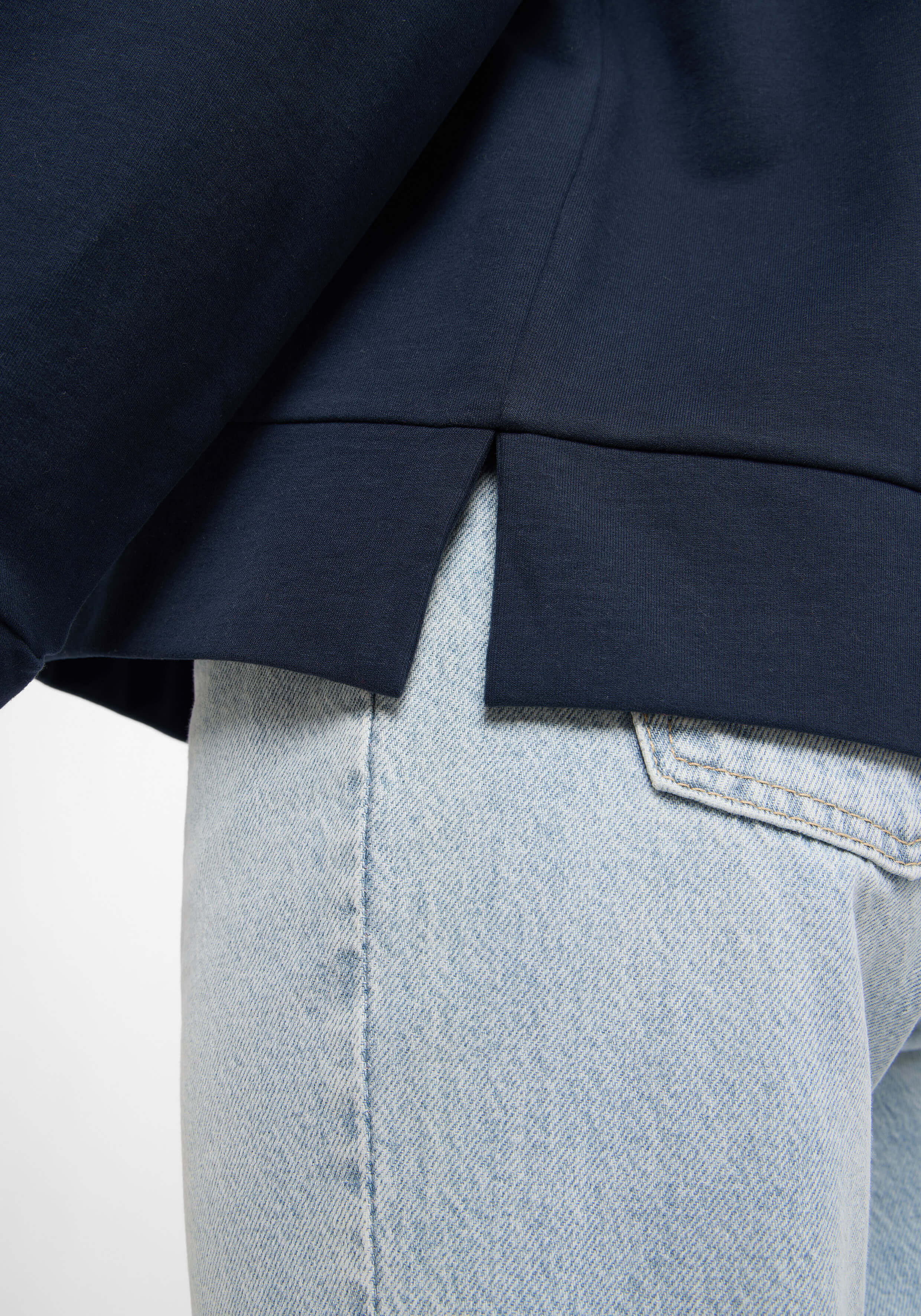 Nahaufnahme eines marineblauen Freizeit-Sweatshirts mit Seitenschlitzen, getragen zu hellblauen Jeans.
