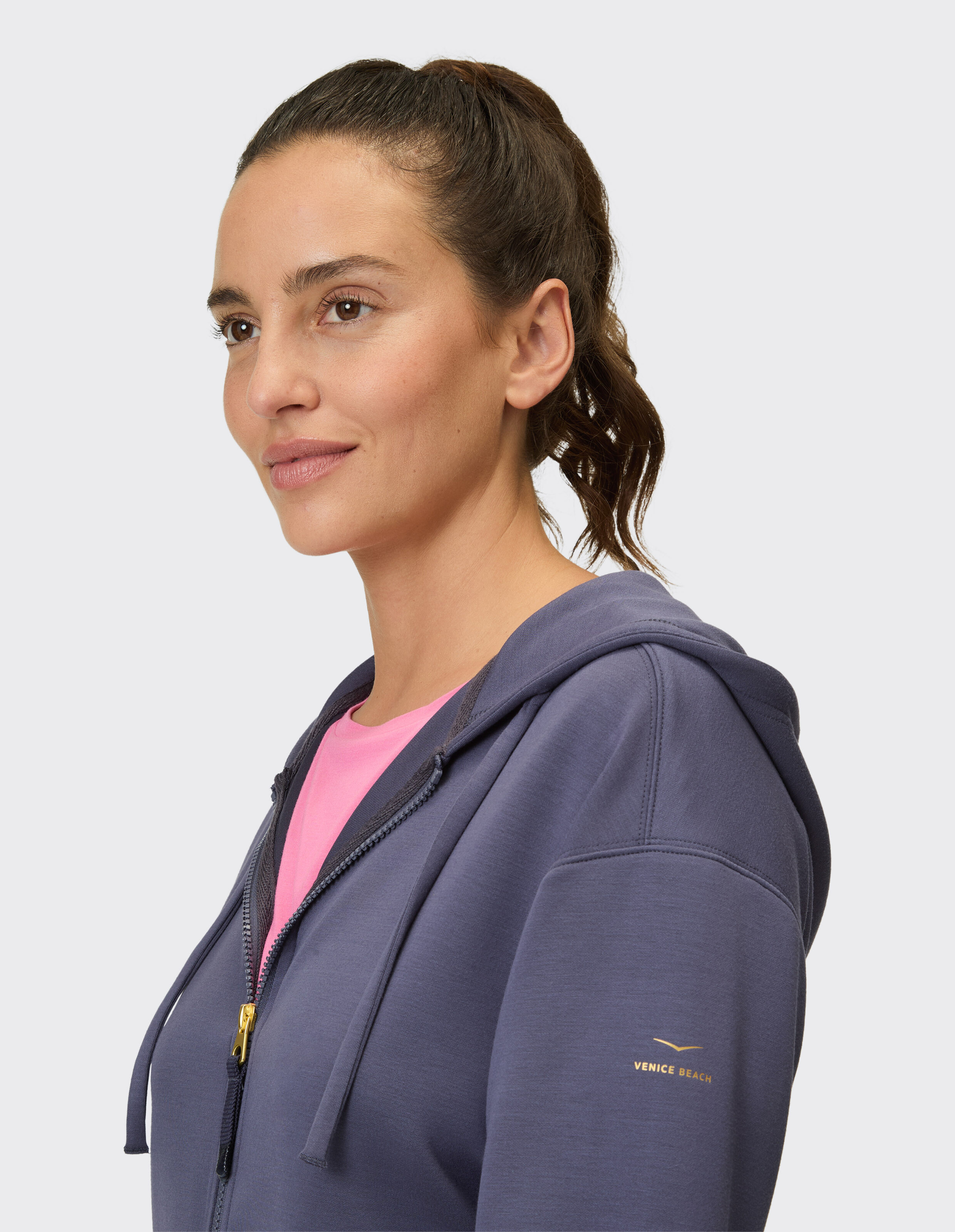 Profilansicht einer Frau in einem dunkelblauen Kapuzenpullover mit einem rosa Hemd darunter.