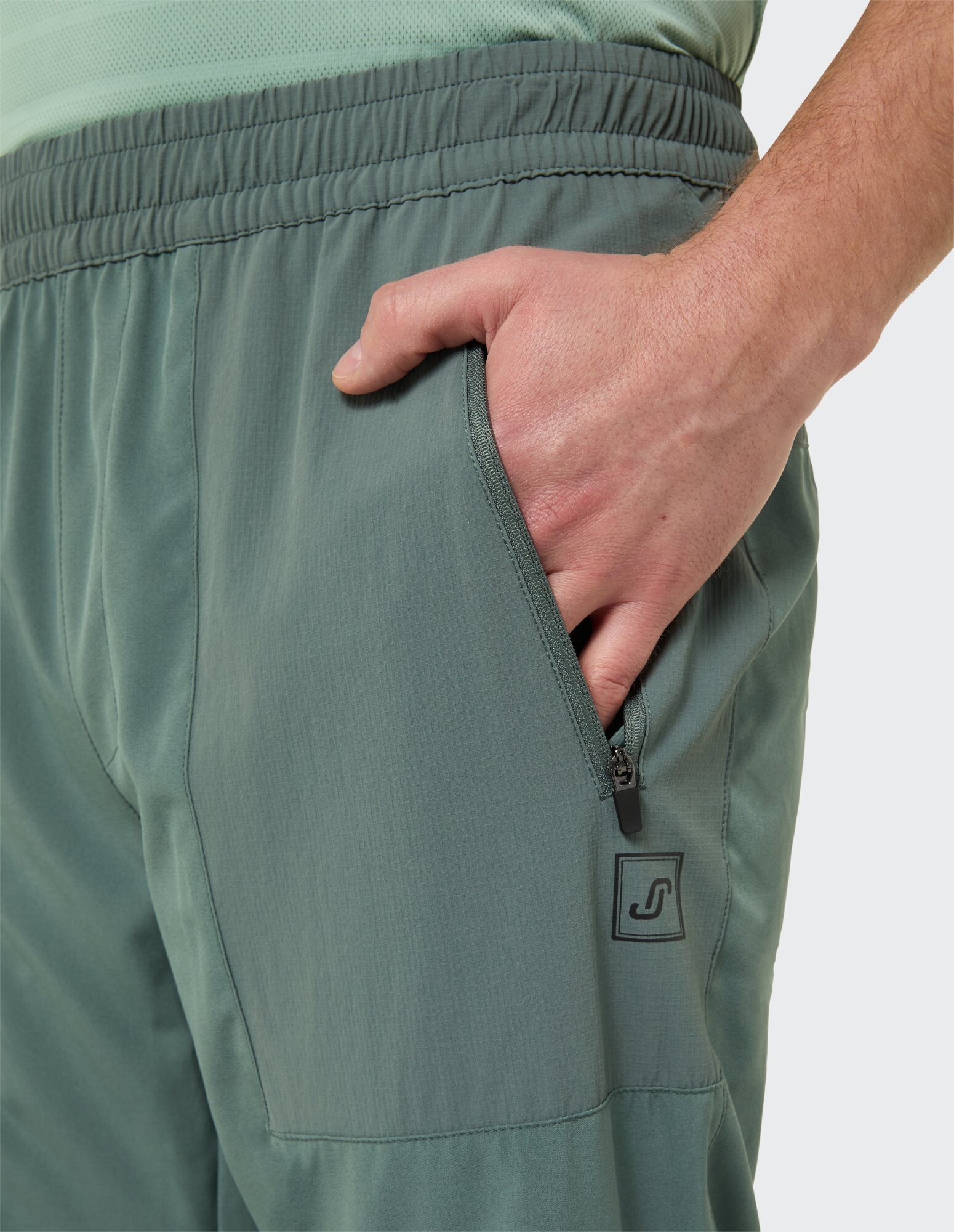 Nahaufnahme einer grünen Freizeithose für Herren mit Reißverschlusstaschendetail.