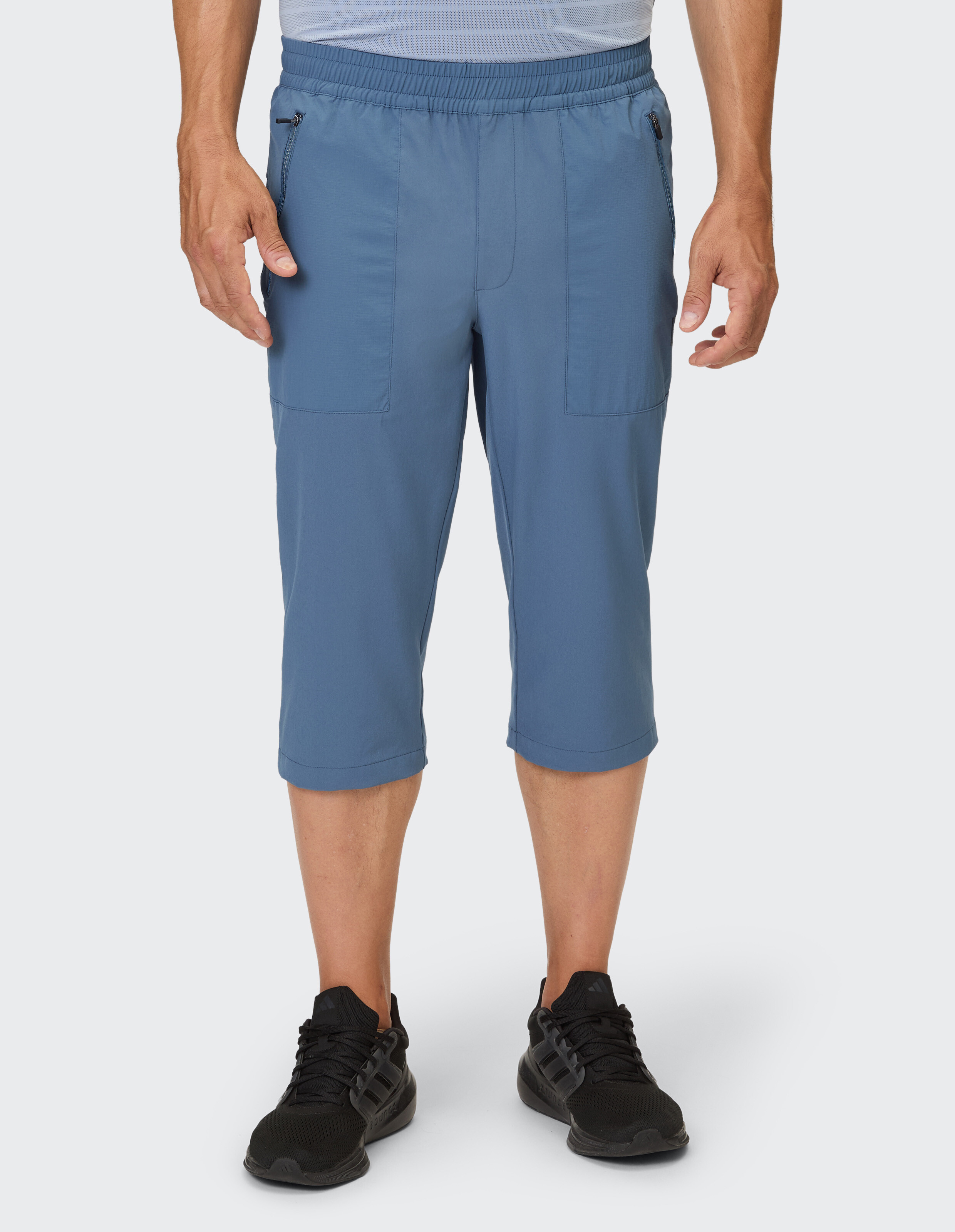 Ein Mann trägt eine blaue Kapri-Hose mit Reißverschlusstaschen und schwarzen Sneakers.