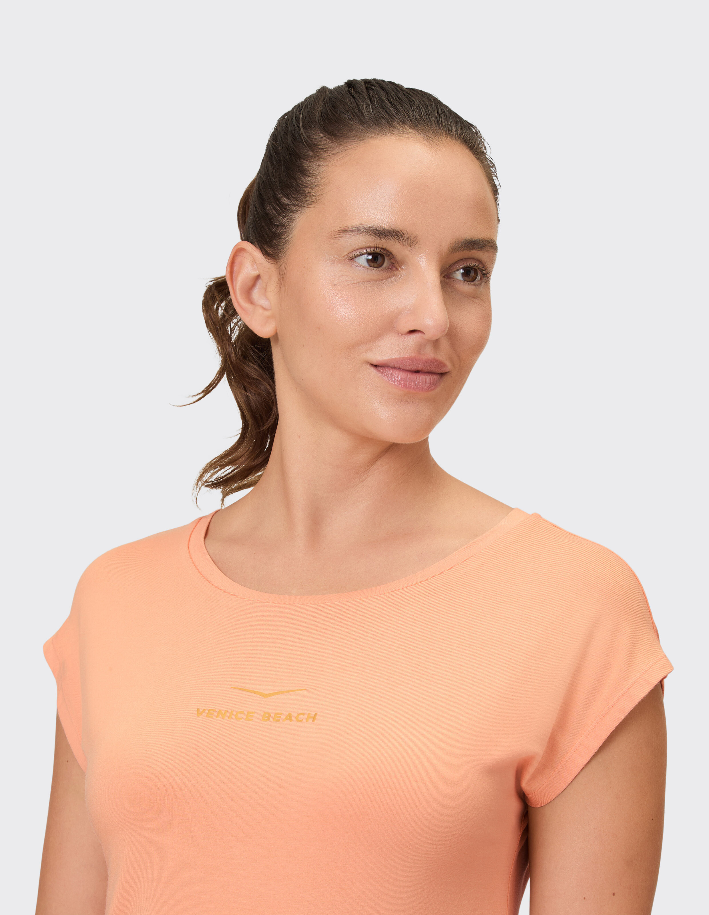 Nahaufnahme einer Frau in einem pfirsichfarbenen Freizeit-T-Shirt mit „Venice Beach“-Logo.