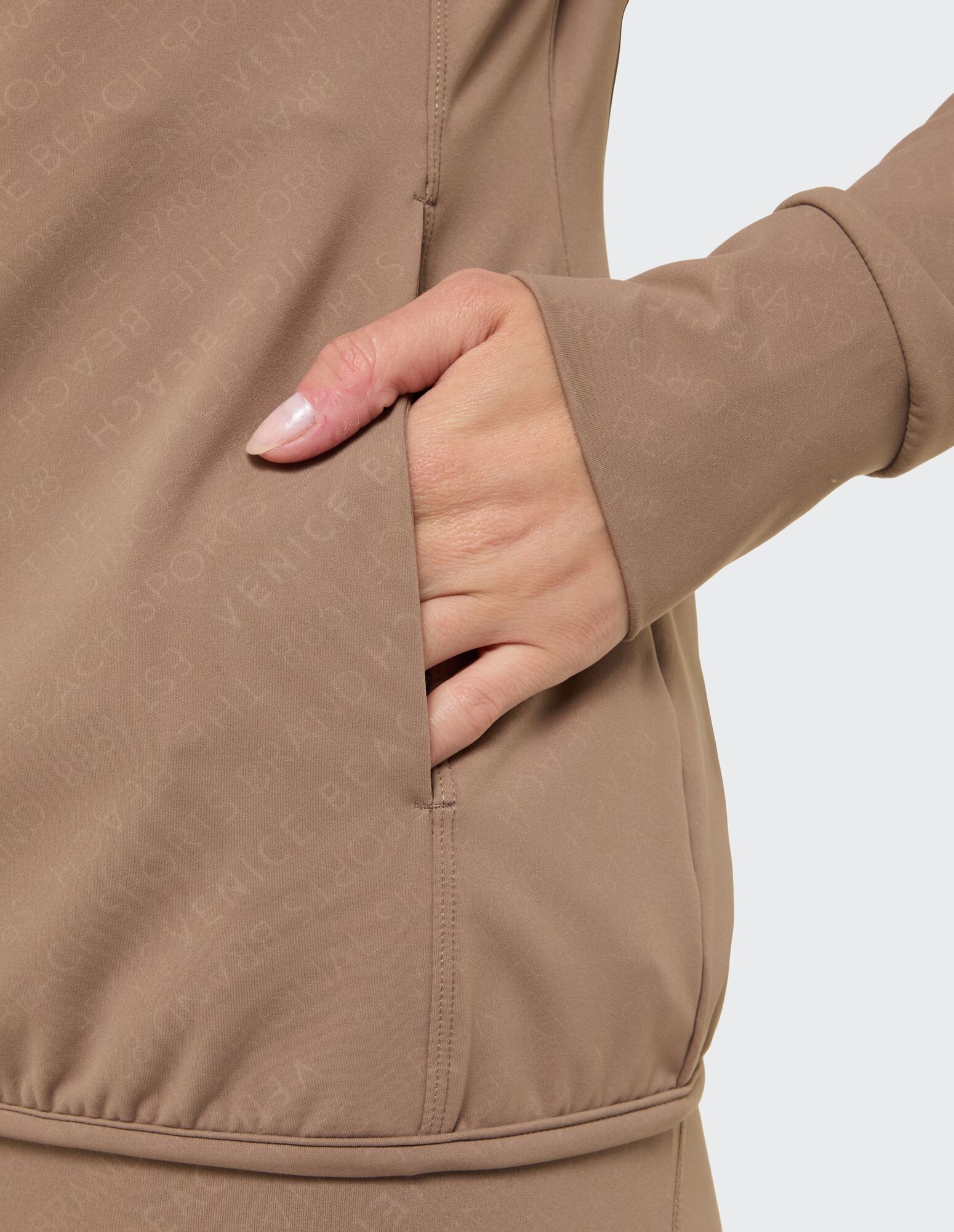 Nahaufnahme einer Hand in der Tasche einer beigen Freizeitjacke mit dezentem Branding.