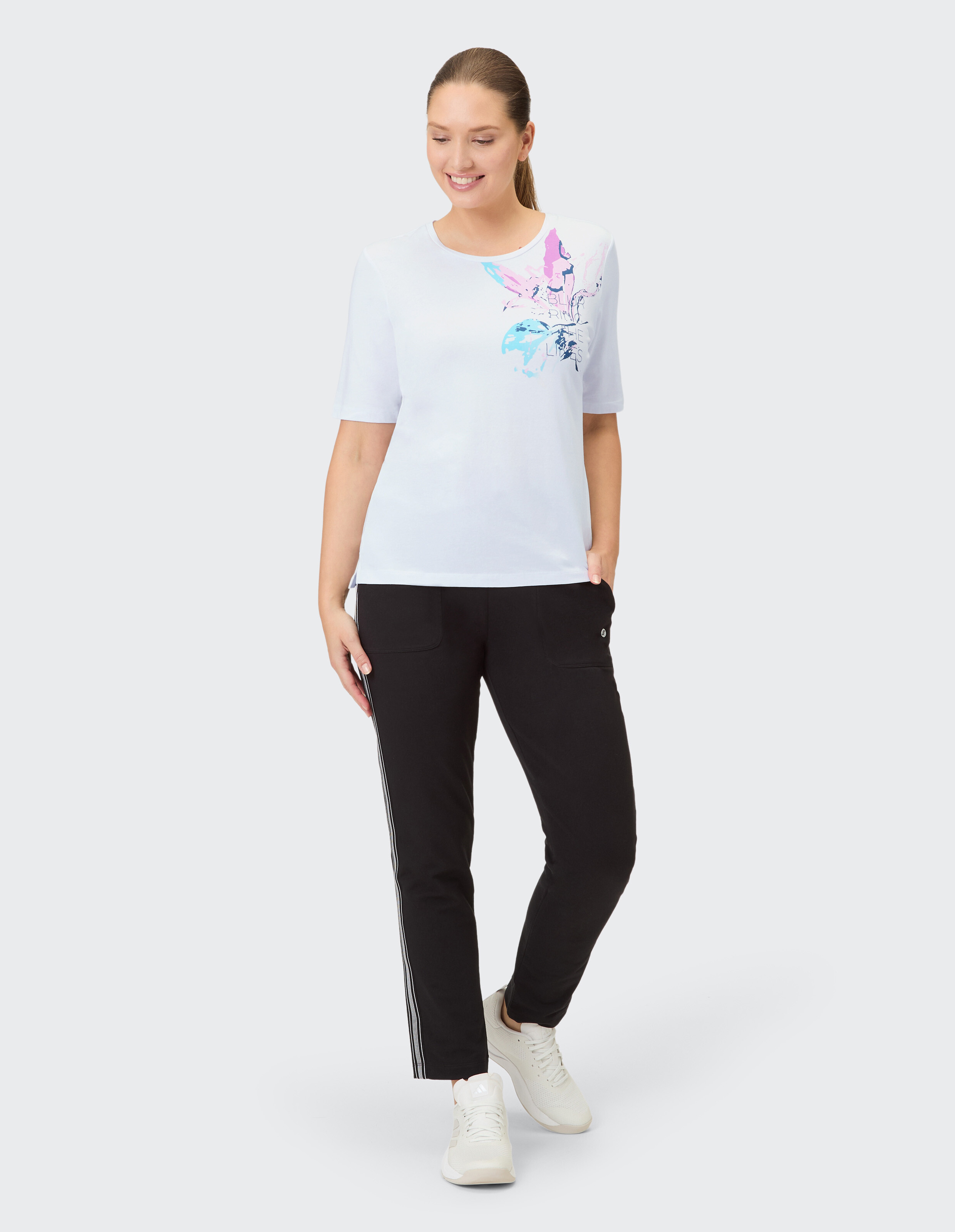 Frau in einem weißen Grafik-T-Shirt und einer schwarzen Hose mit Streifen, ideal für Freizeitkleidung.