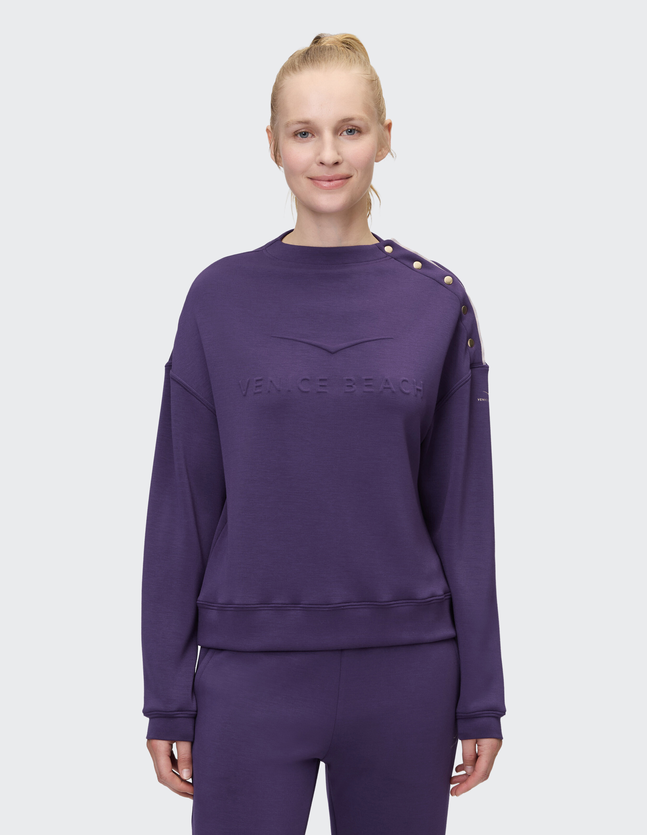 Frau trägt ein gemütliches lila ELBSAND-Sweatshirt mit goldenen Schulterknöpfen.