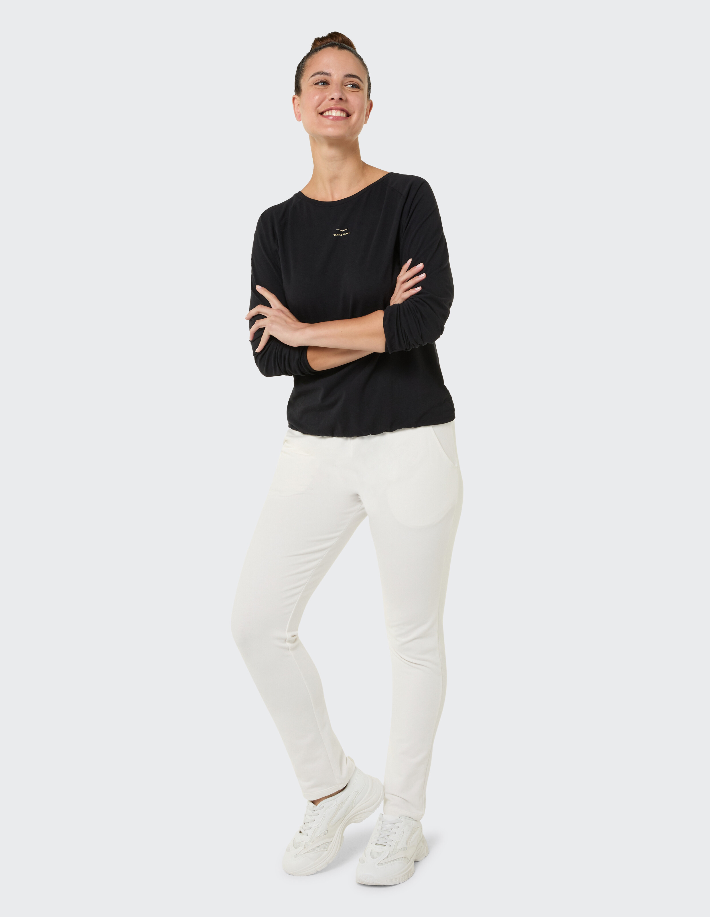 Frau trägt ein schwarzes Langarmshirt und eine weiße Freizeithose für einen bequemen, stilvollen Look.