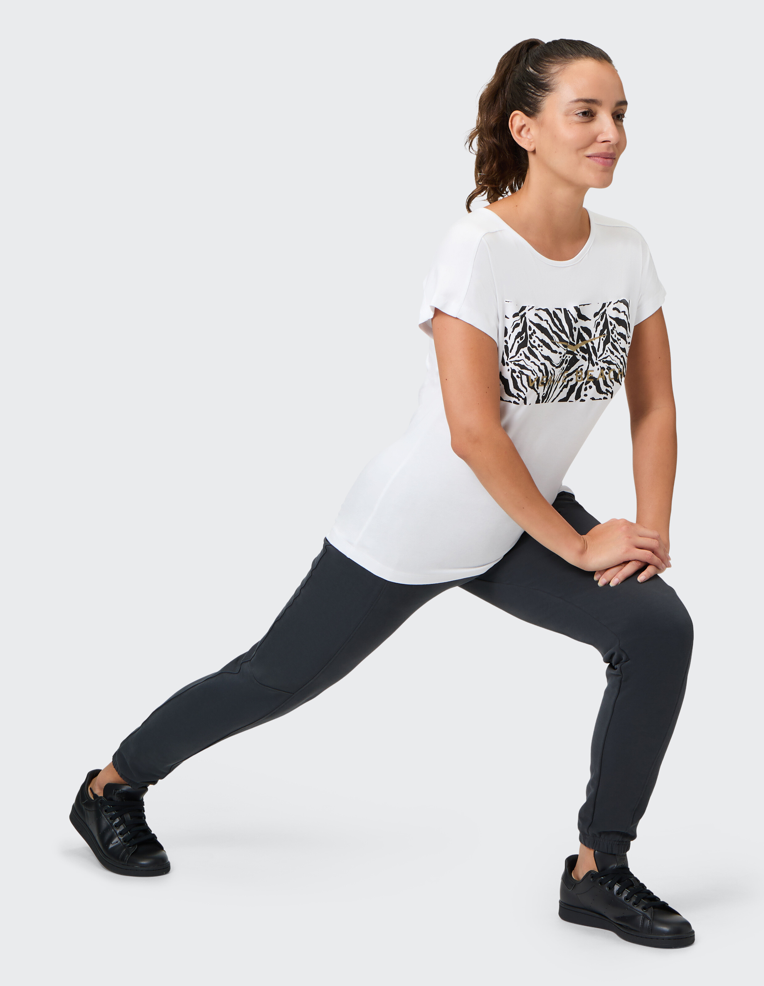 Frau in weißem T-Shirt mit Zebramuster und dunkler Jogginghose beim Stretching für Freizeitkleidung.