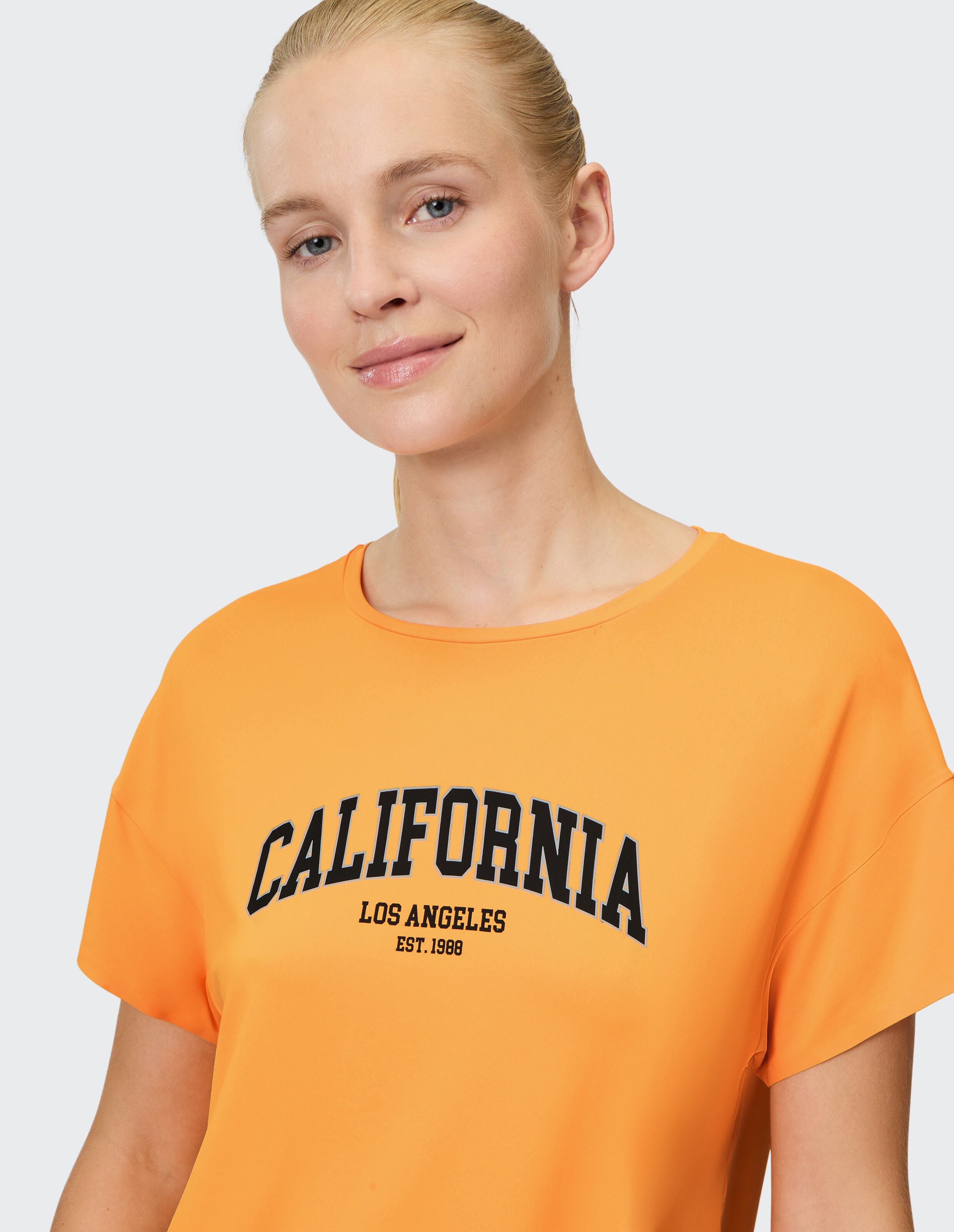 Frau trägt ein orangefarbenes, lässiges Kurzarmhemd von Venice Beach Edana.