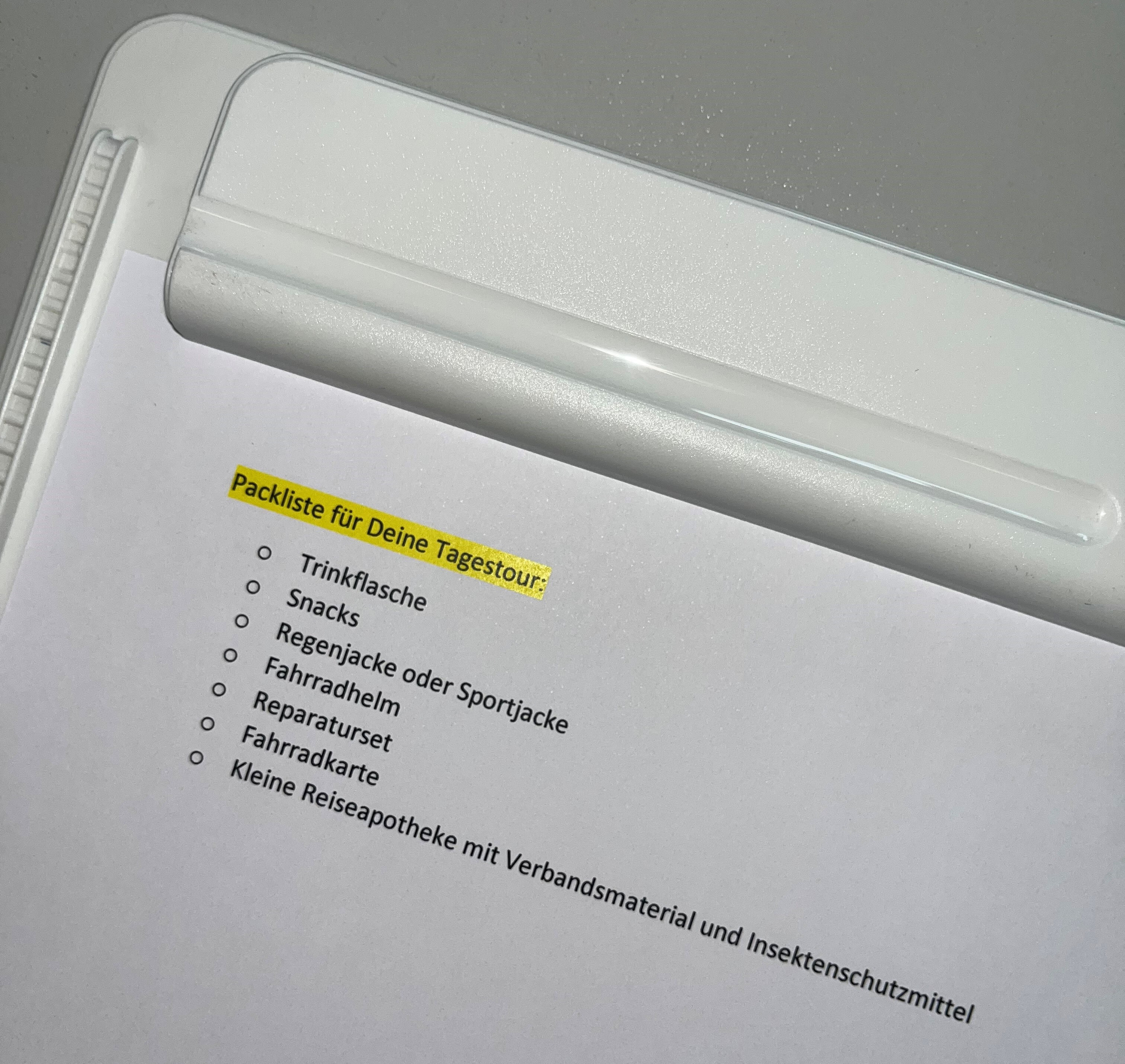 Packliste auf Klemmbrett: Trinkflasche, Snacks, Regenjacke, Helm, Reparaturset, Karte und Reiseapotheke mit Verbandsmaterial.