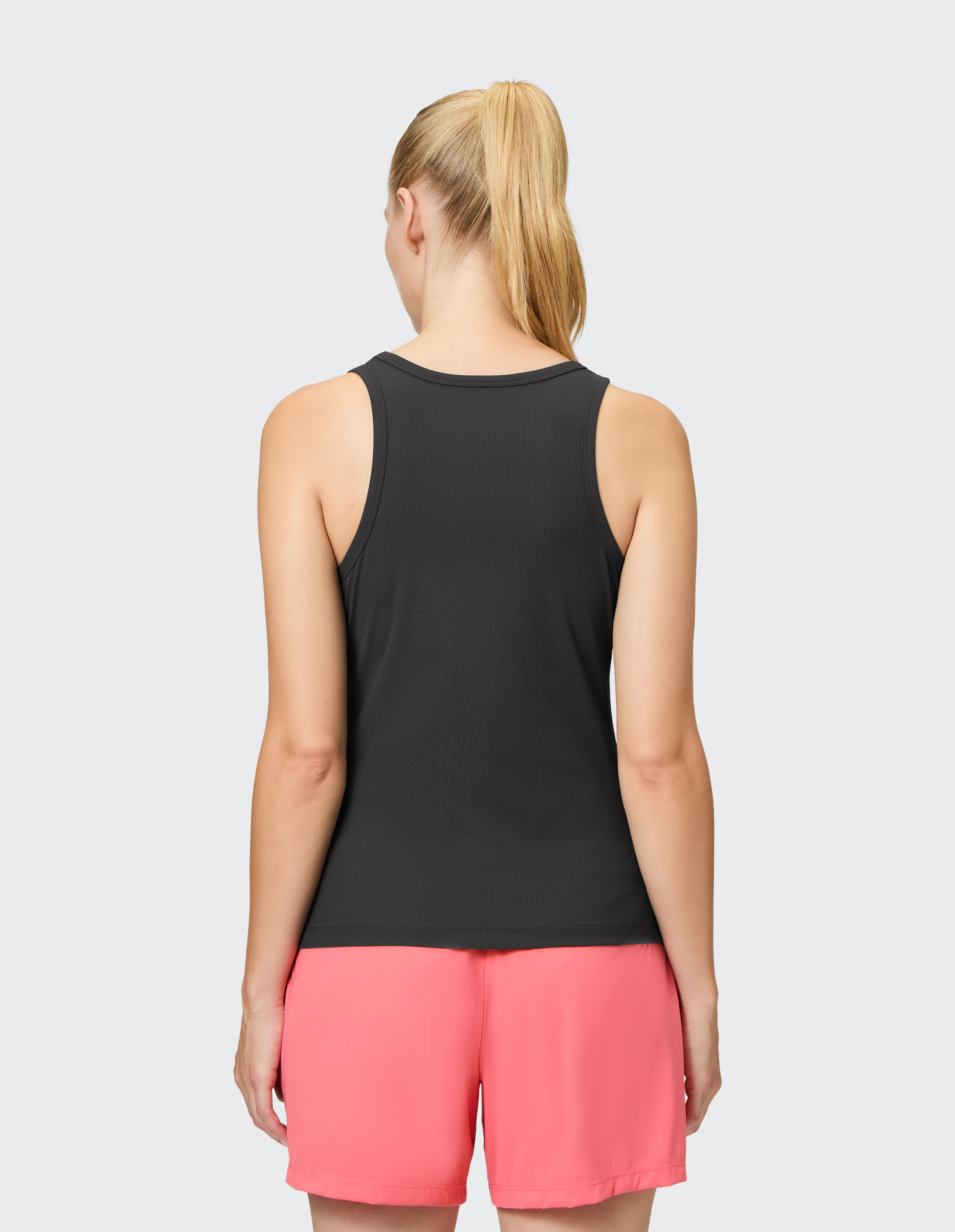 Frau trägt ein schwarzes Tanktop und korallenrote Shorts, Rückansicht, lässiger Lounge-Stil.