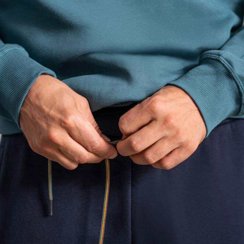 Nahaufnahme von Händen, die den Kordelzug an einer dunkelblauen Jogginghose mit einem blaugrünen Sweatshirt anpassen.