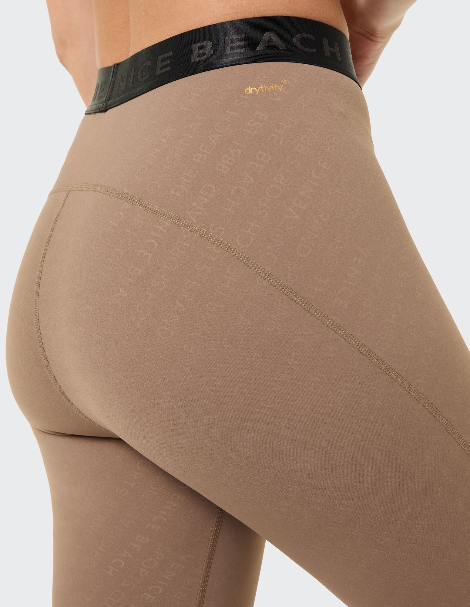 Nahaufnahme einer beigen Leggings mit schwarzem Bund und dezentem Logomuster.