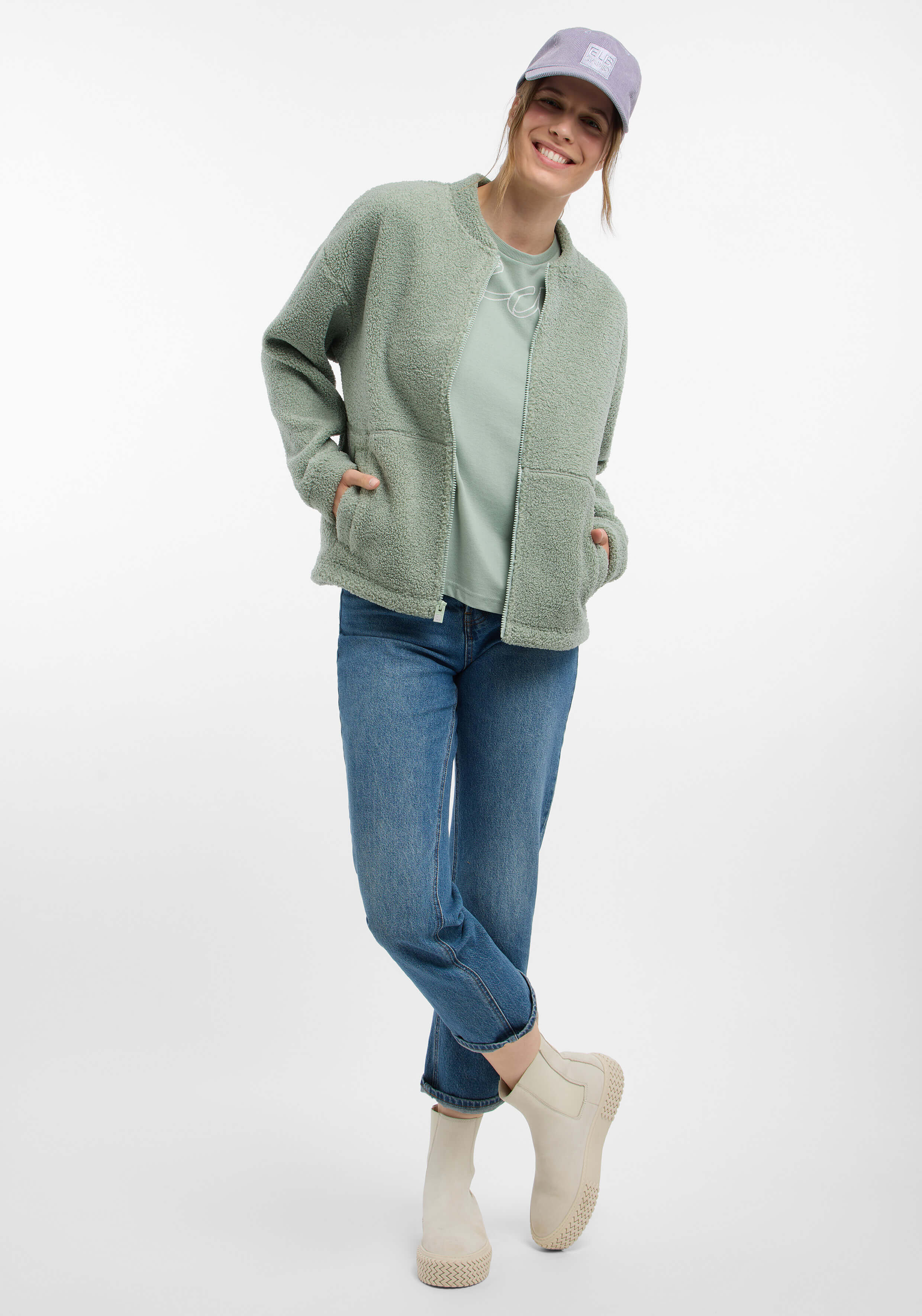 Frau in gemütlicher grüner Fleecejacke und hellem Hemd, gepaart mit Jeans und Stiefeln.