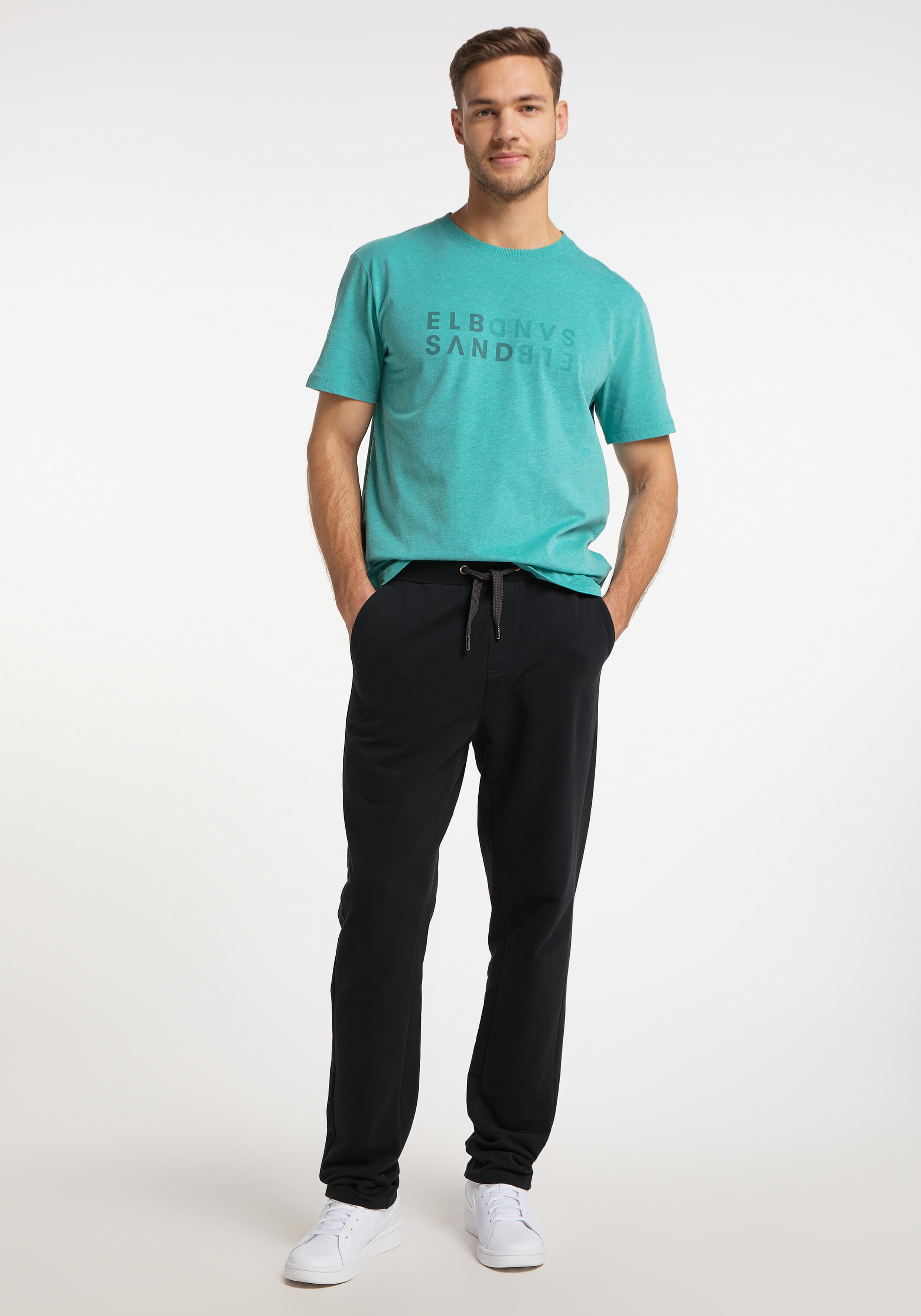 Mann trägt ein grünes T-Shirt mit ELBSAND-Logo und eine schwarze Freizeit-Jogginghose.