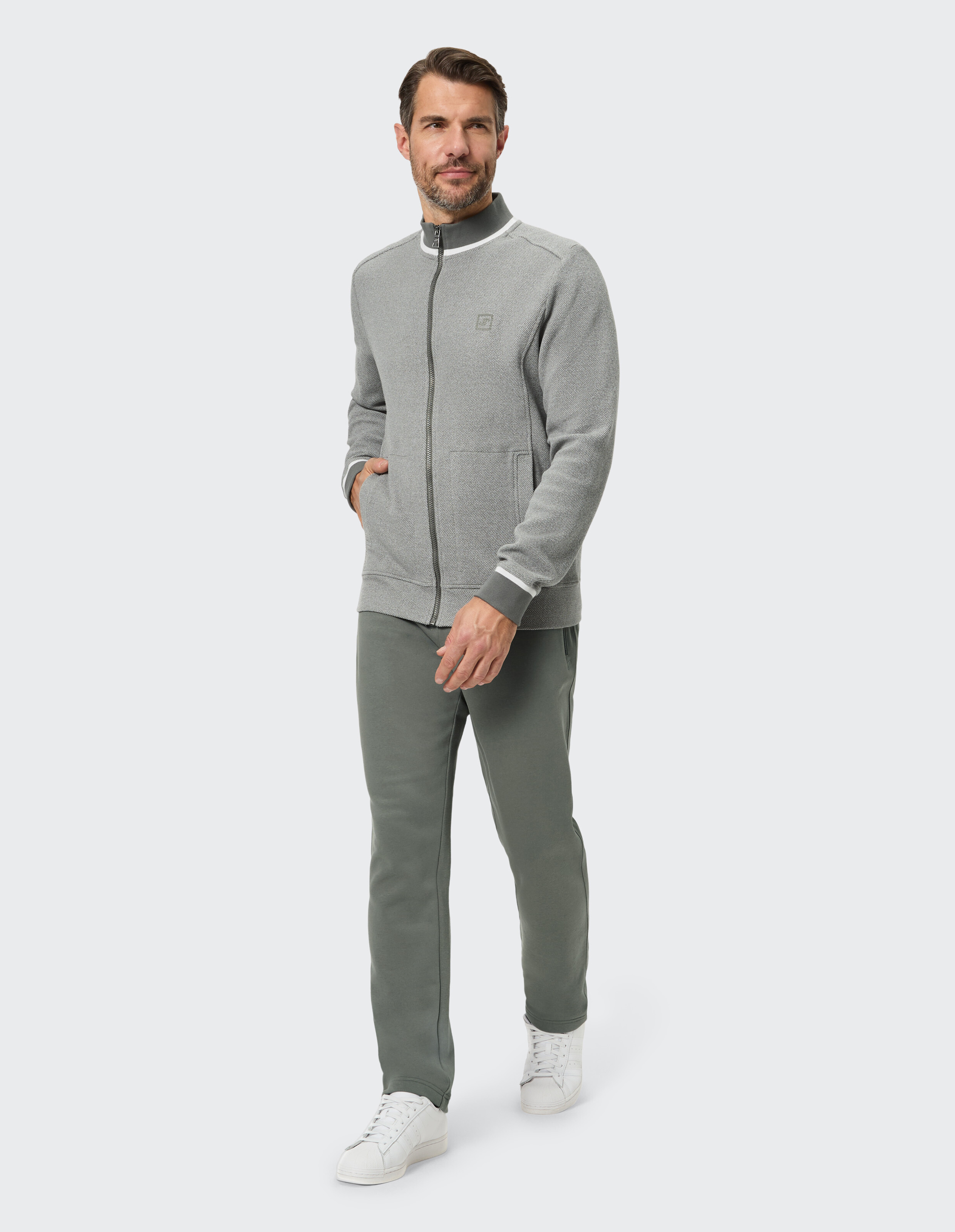 Mann in einer grauen Jacke mit Reißverschluss und einer grünen Hose, perfekt für Freizeitkleidung.