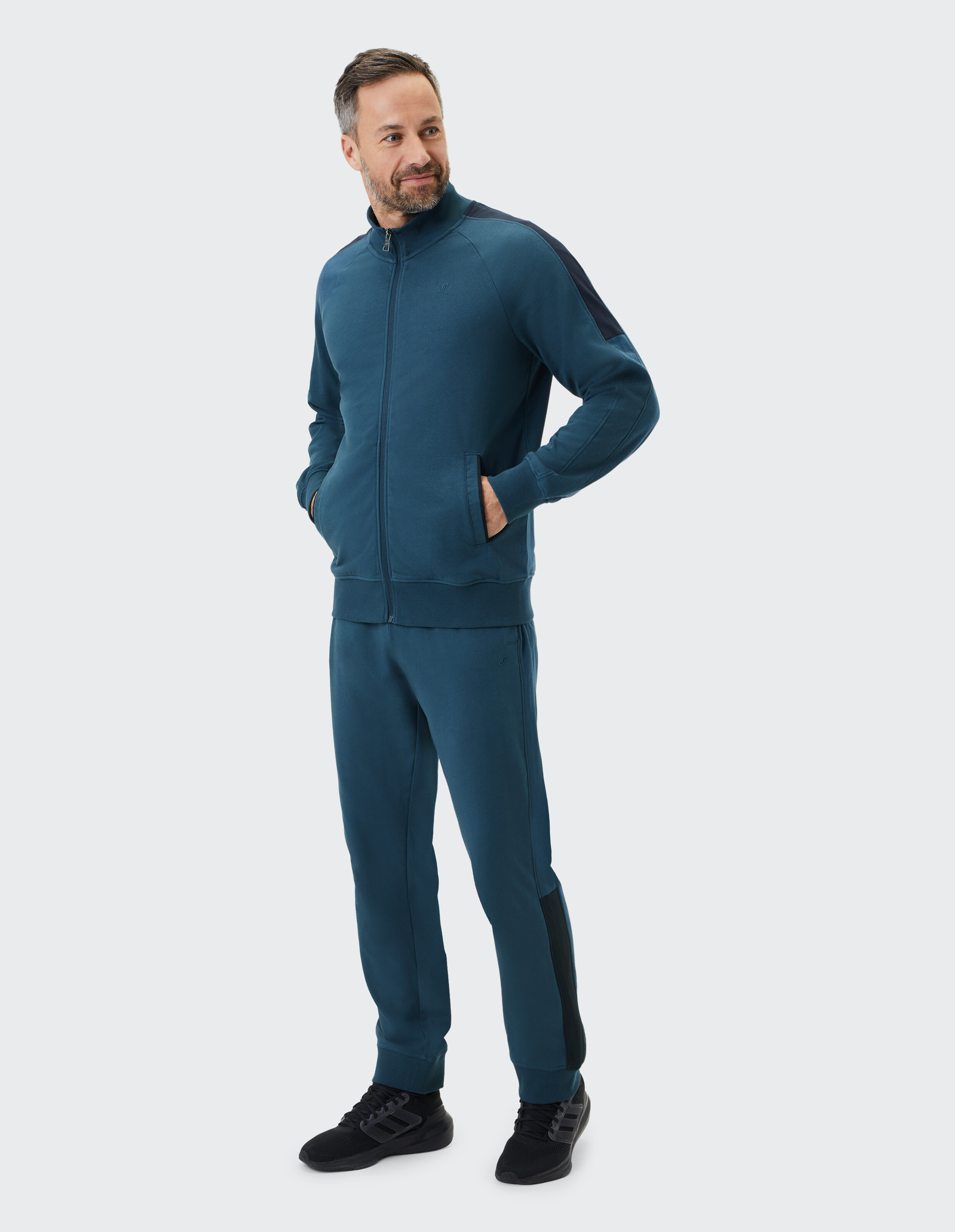 Blauer Trainingsanzug mit Reißverschlussjacke und langen Ärmeln, Hose mit elastischem Bund, schwarze Akzente an Schultern und Seiten.