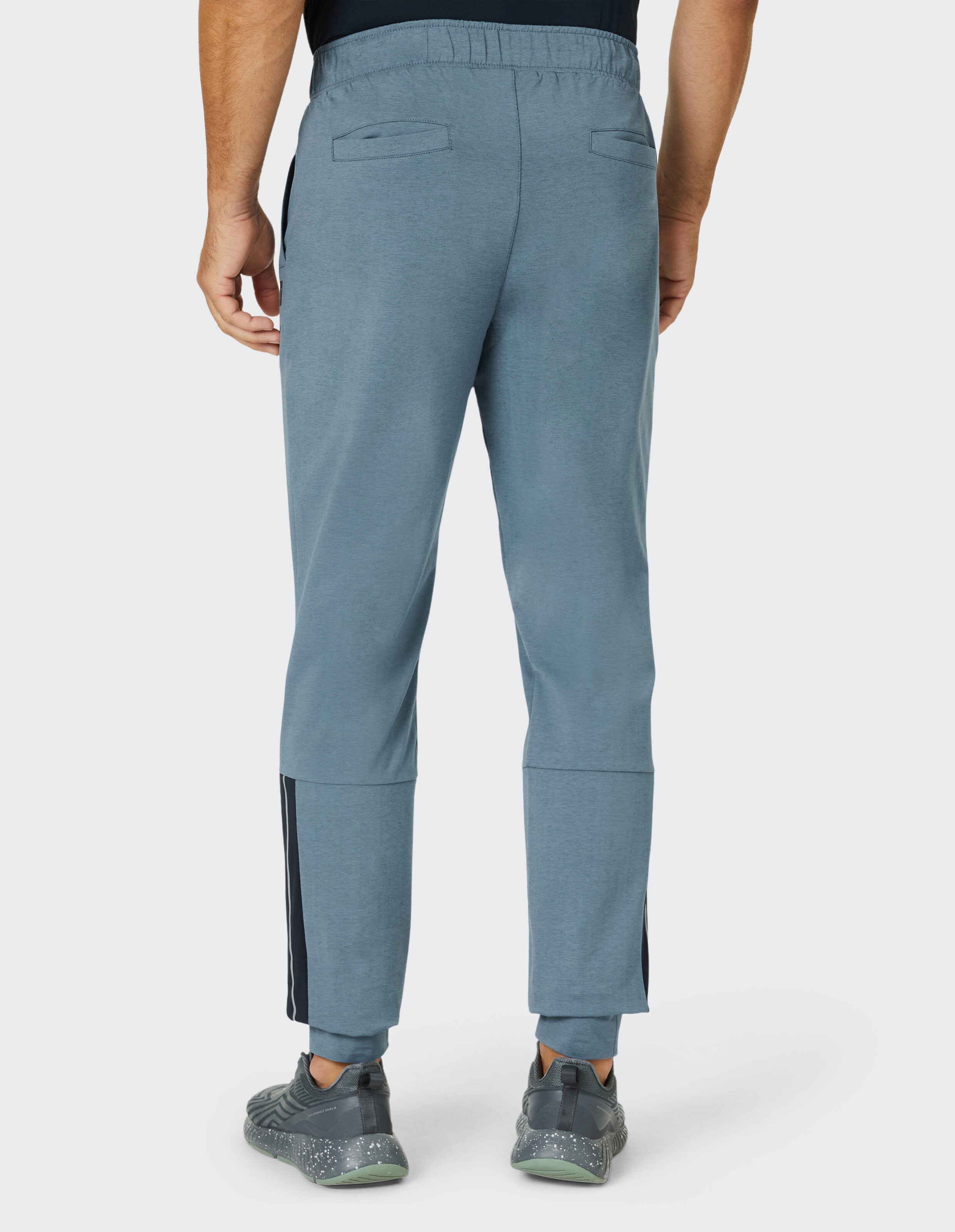 Rückansicht eines Mannes in blauer Jogginghose mit elastischem Bund, schwarzen Streifen an den Seiten und grauen Sneakers.