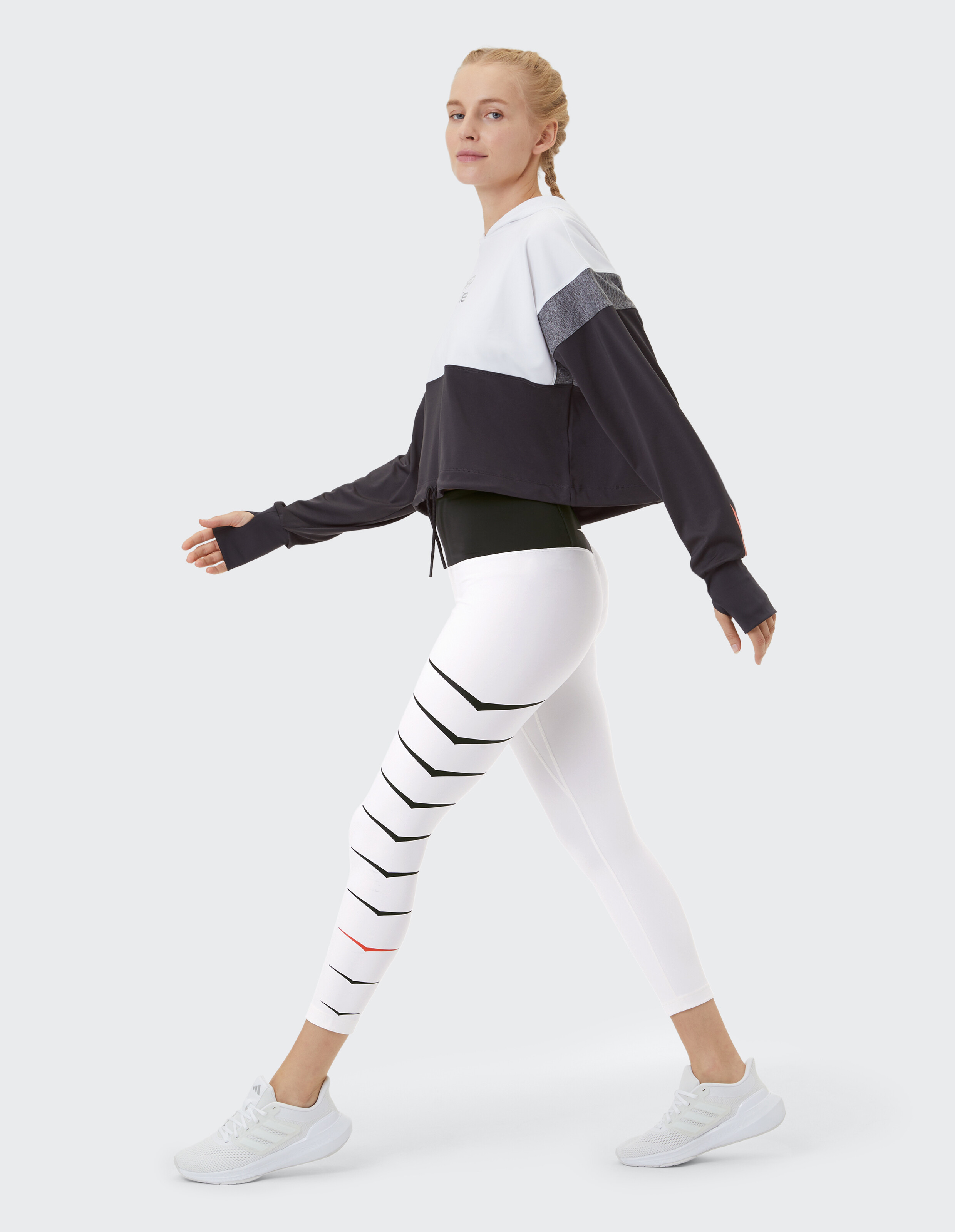 Frau in einem kurzen Kapuzenpullover in Colour-Block-Optik und gestreiften Leggings, ideal für Freizeitkleidung.