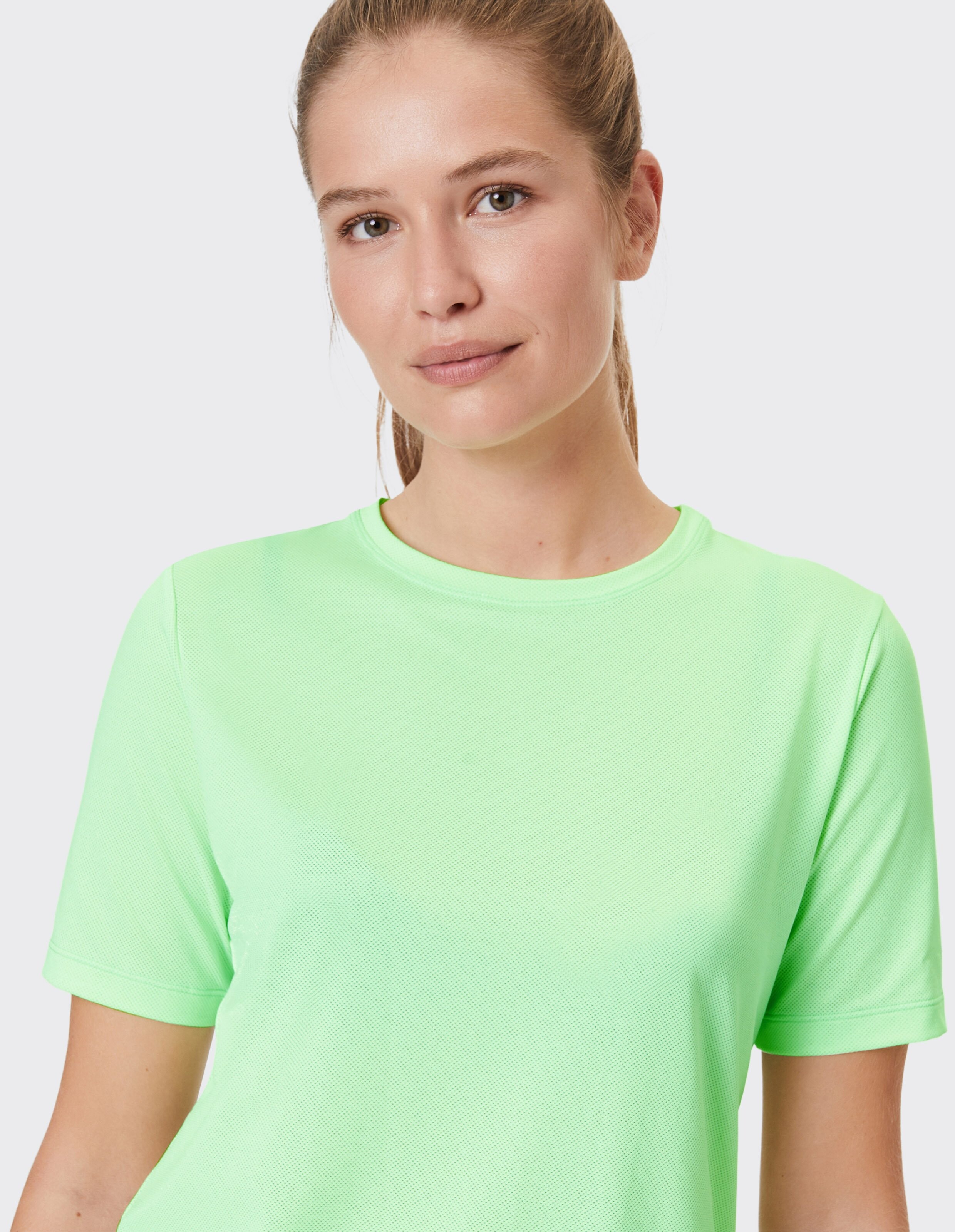 Nahaufnahme einer Frau, die ein hellgrünes Kurzarm-T-Shirt trägt.