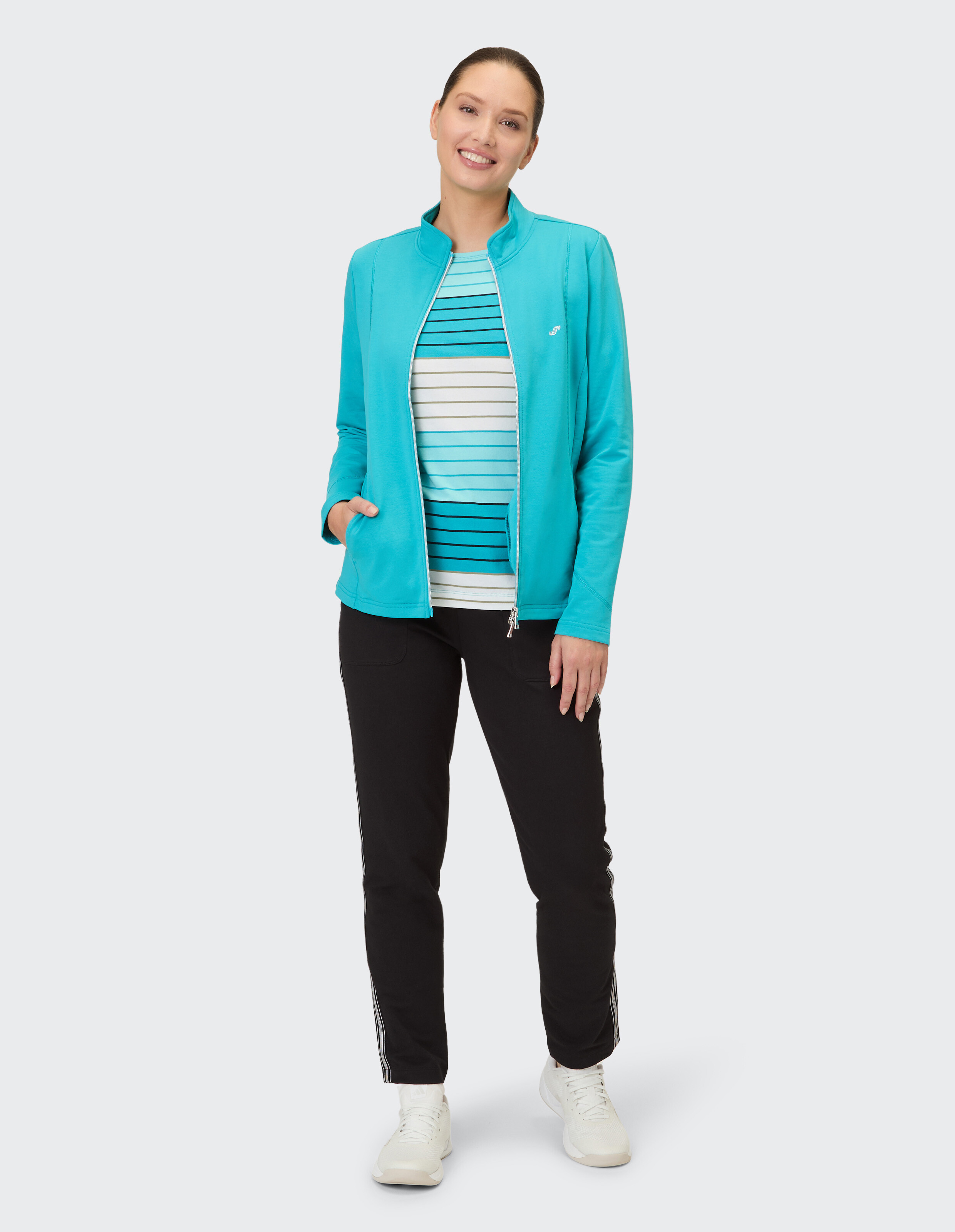 Frau in einer türkisfarbenen Jacke über einem gestreiften Oberteil und einer schwarzen Hose, gestylt für Freizeitkleidung.