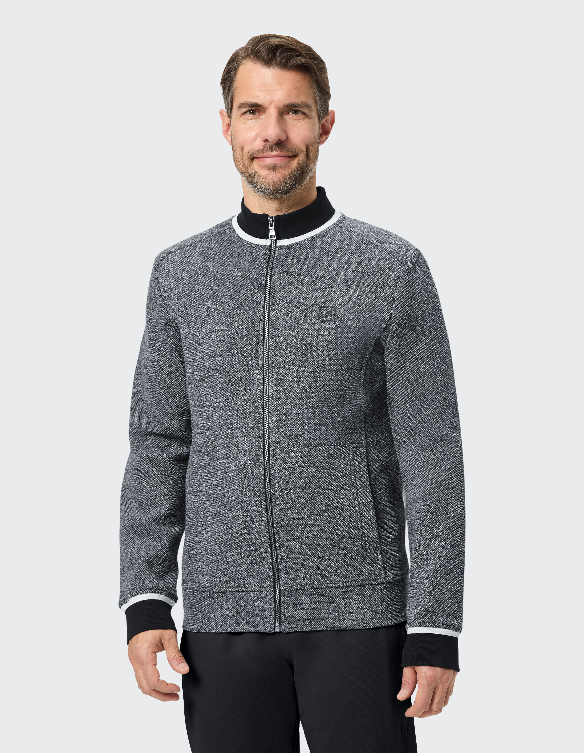 Ein Mann trägt eine graue Strickjacke mit durchgehendem Reißverschluss, einem schwarzen Kragen mit weißem Rand und schwarzen Ärmelbündchen.