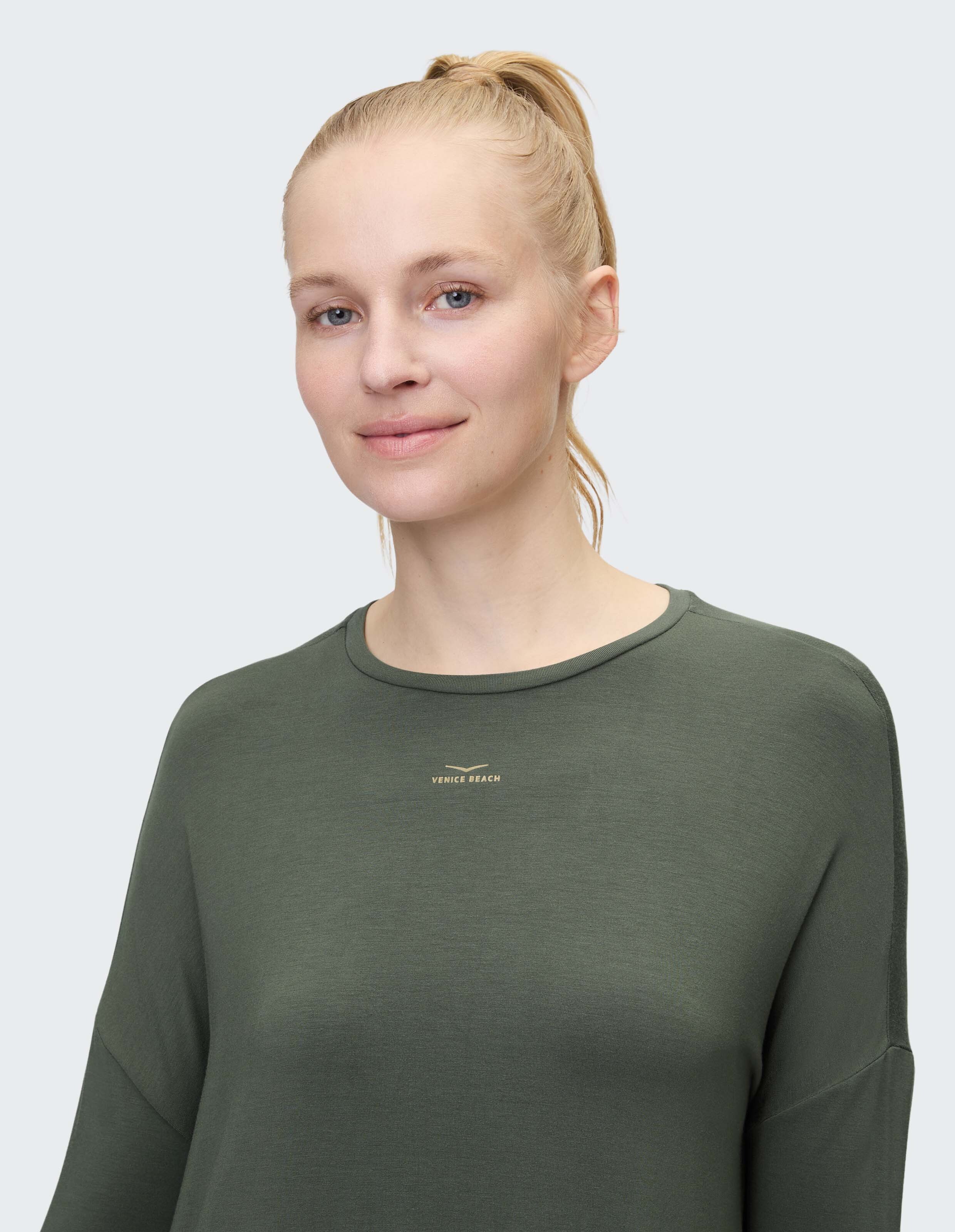 Frau trägt ein gemütliches olivgrünes Langarmshirt mit dezentem Logo.