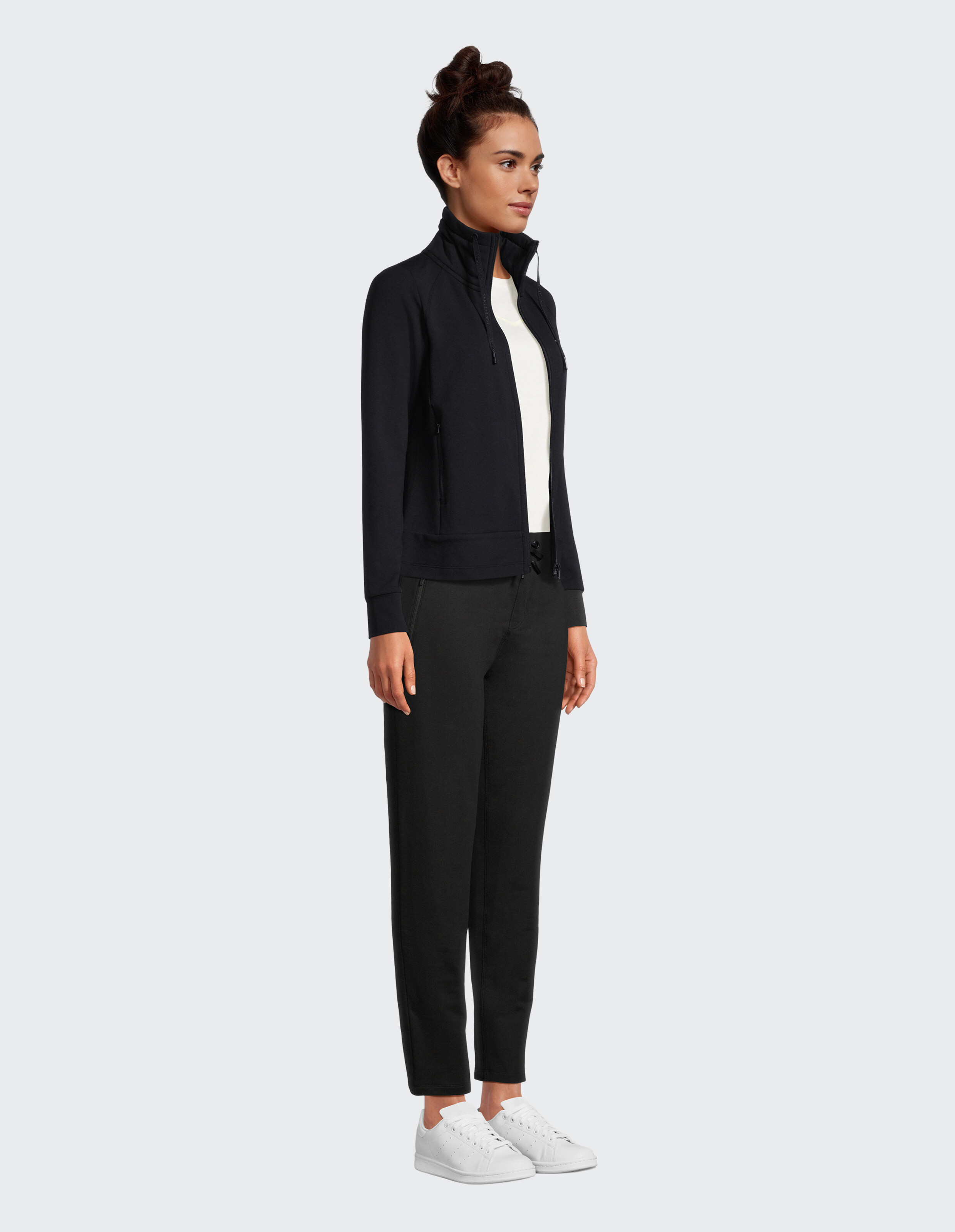 Frau in einer schwarzen Jacke mit Reißverschluss und einer schwarzen Hose, gestylt für lässigen Komfort.