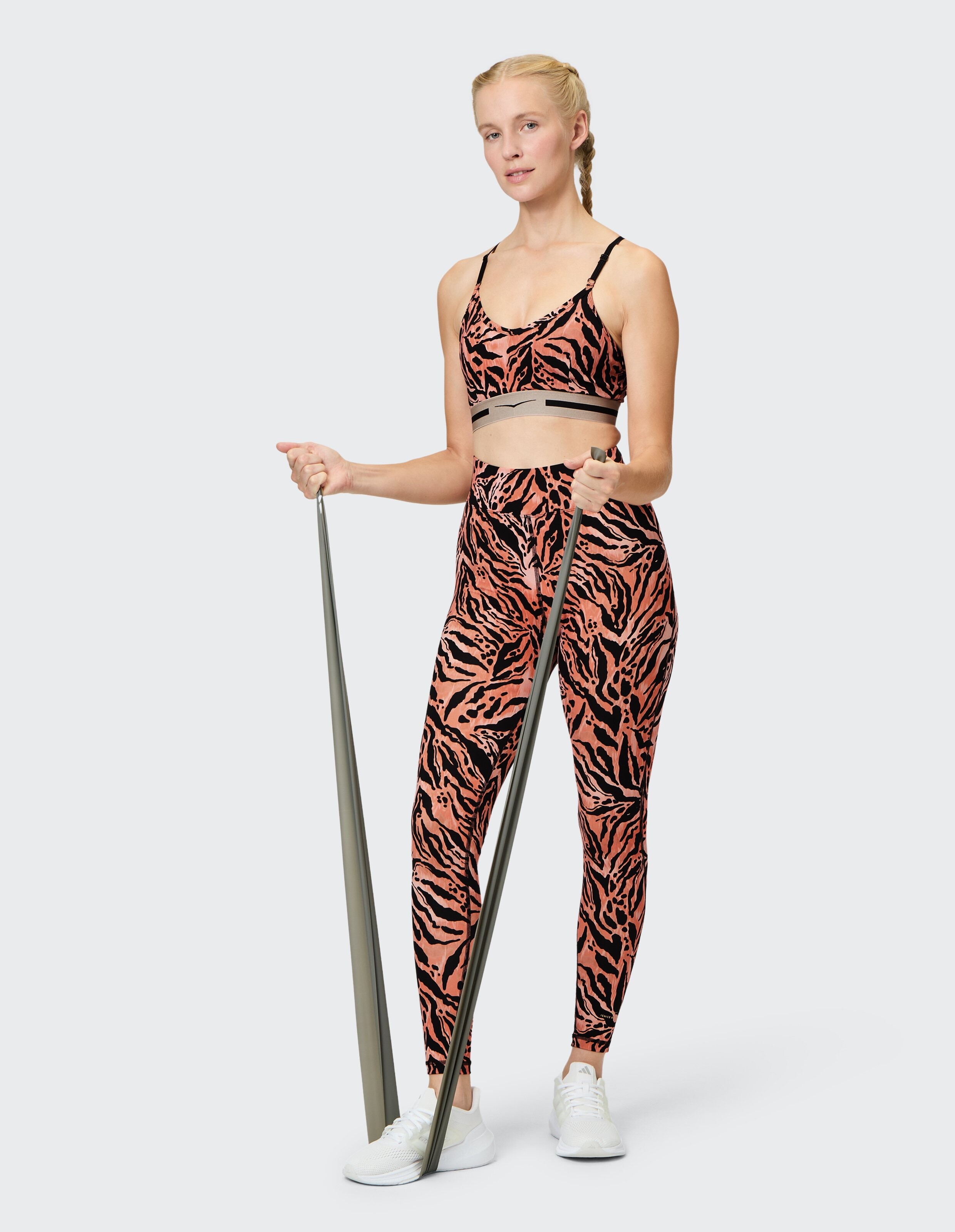 Frau trägt Top Oakley und passende Leggings mit orangefarbenem Tigerprint für lässige Workouts.